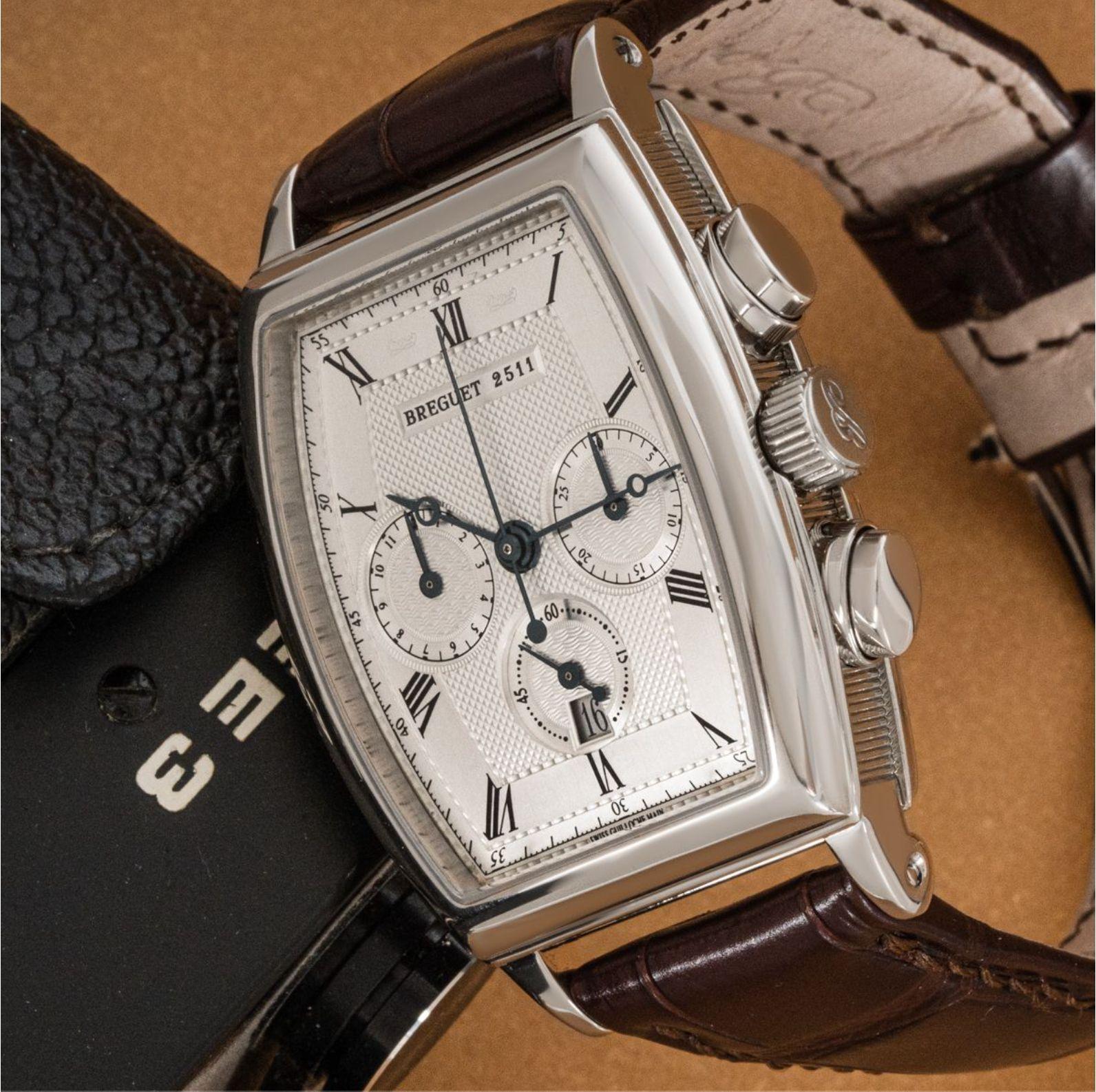 A white gold Breguet chronograph from the Heritage collection. The tonneau shaped case features a silver dial with roman numerals, blue steel moon hands, 3 chronograph counters and a white gold bezel.

Presented on a Breguet brown leather strap and