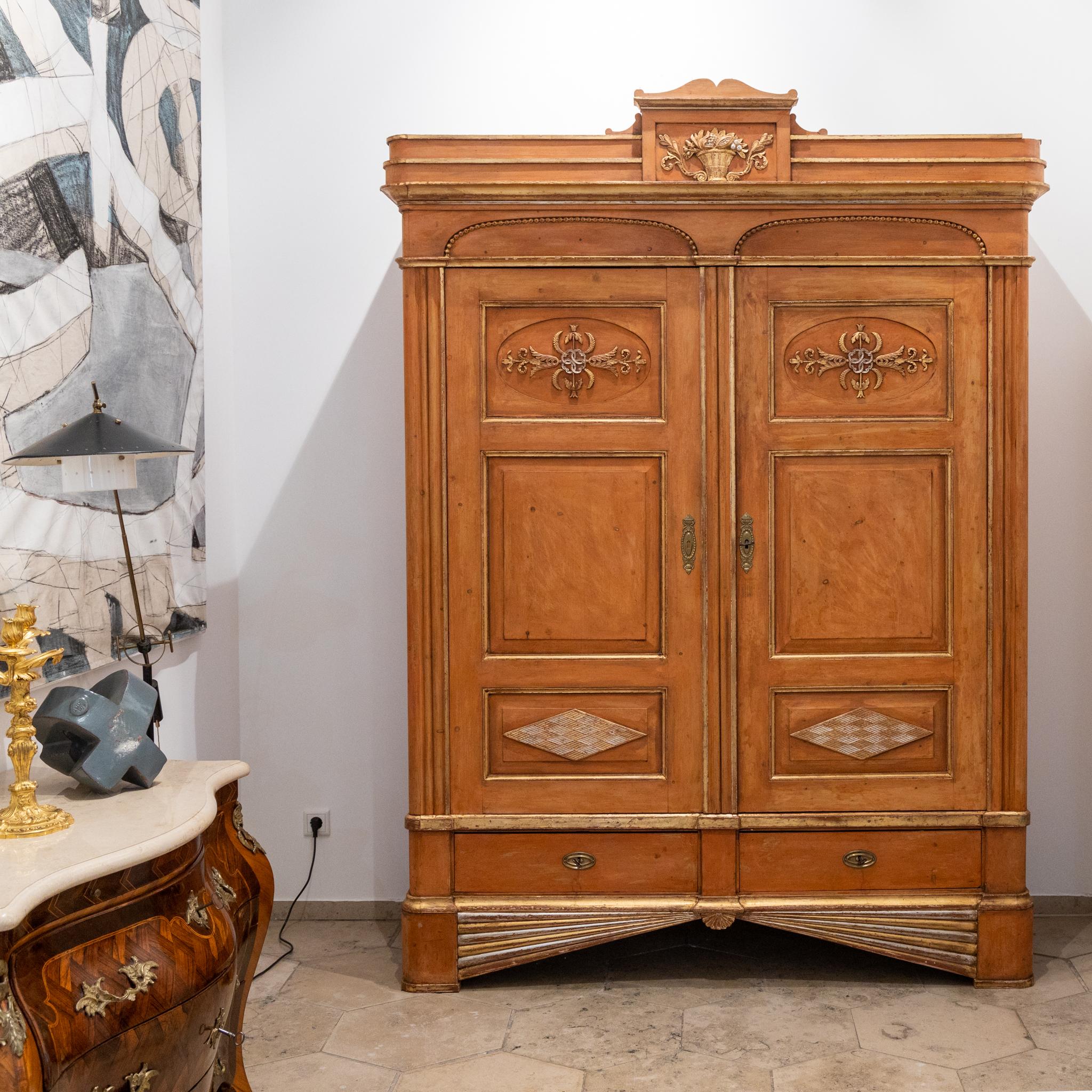 Large beveled cabinet with two doors and two drawers and gold and silver patinated stucco decorations in the form of vines and fruit baskets.