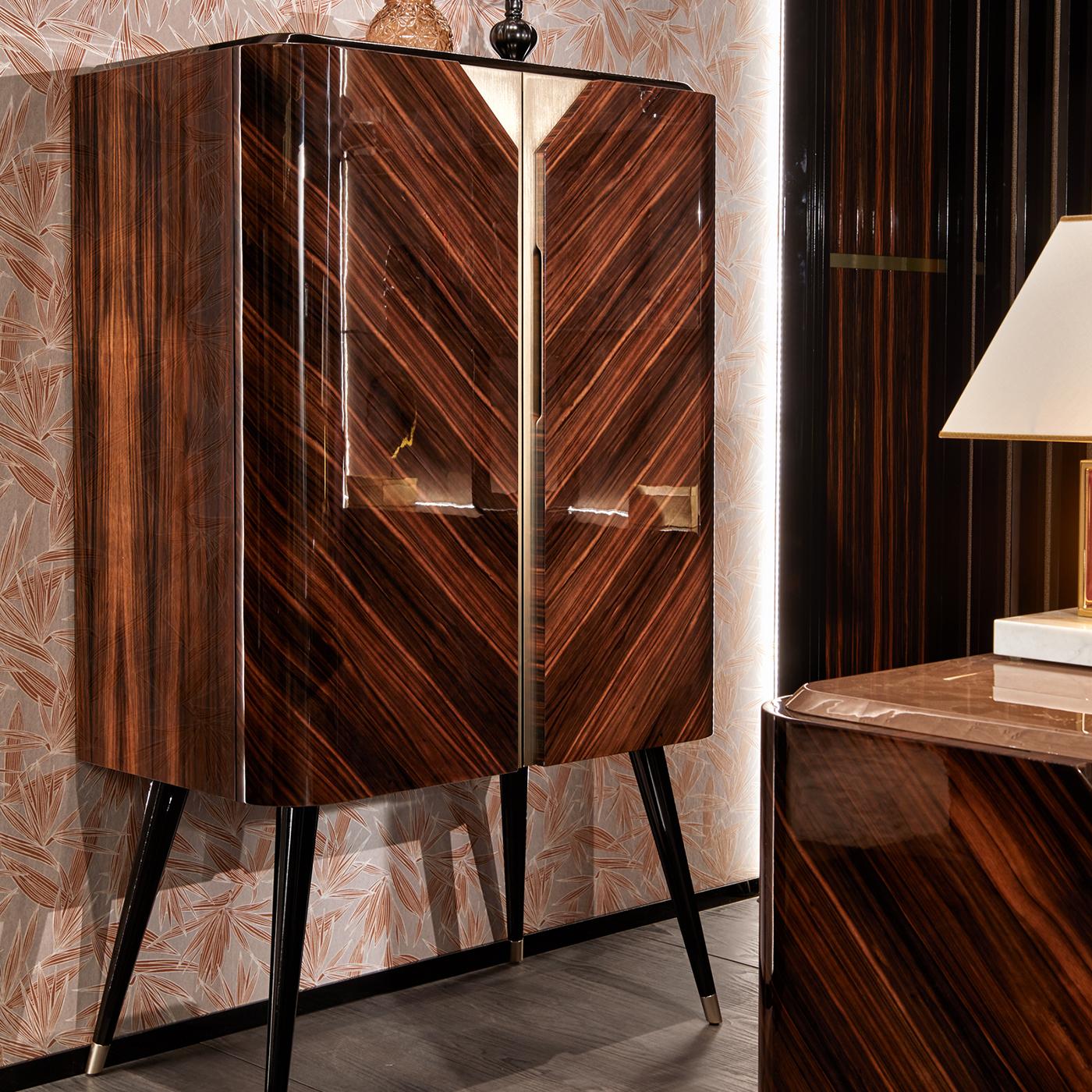 Testament to the beauty of natural wood, the Brent Bar Cabinet is made in stunning Macassar ebony, with carefully placed panels that exalt the wood's veins. Standing on flared legs inspired by Mid-Century Modern designs, the bar cabinet with a