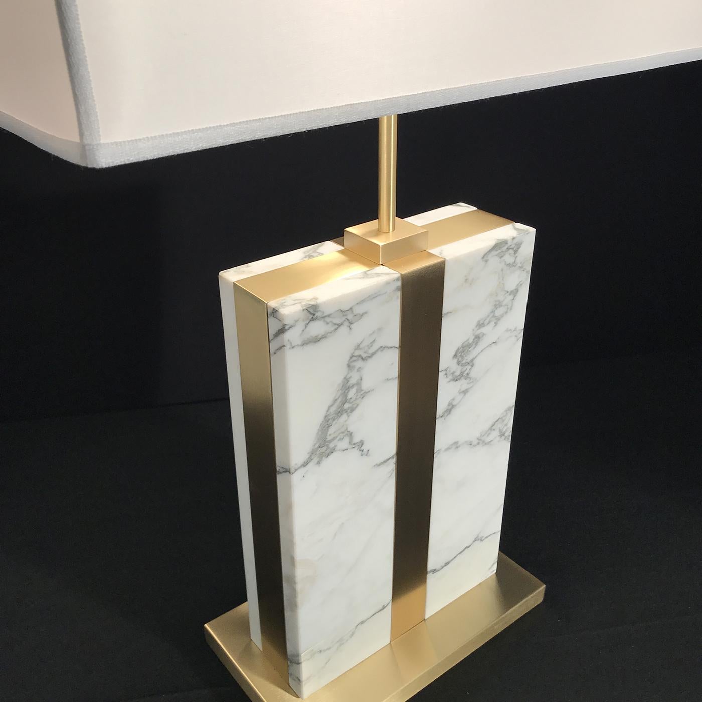 Precious materials work in unison to deliver the elegant silhouette of this modern table lamp. Enclosed in a satin brass frame and raised on a square base, the superb Arabascato Carrara marble draws in the focus while reflecting a warm glow from the