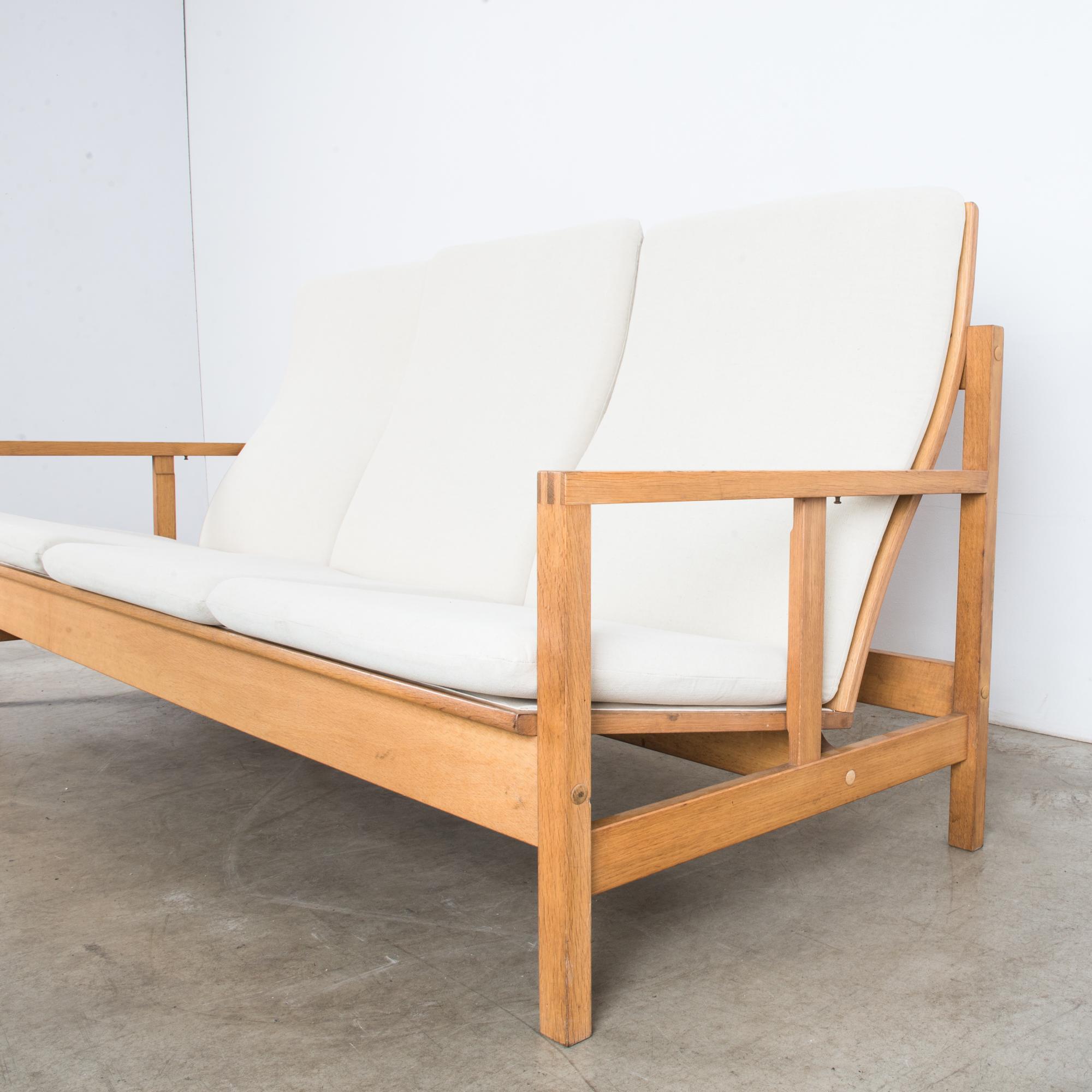 This three-seater sofa with an oak frame was made in Denmark, circa 1960. The clean lines of the frame and ergonomic backrest with the curved splats reflect the timeless elegance of Danish Modern design and its emphasis on both form and function. A