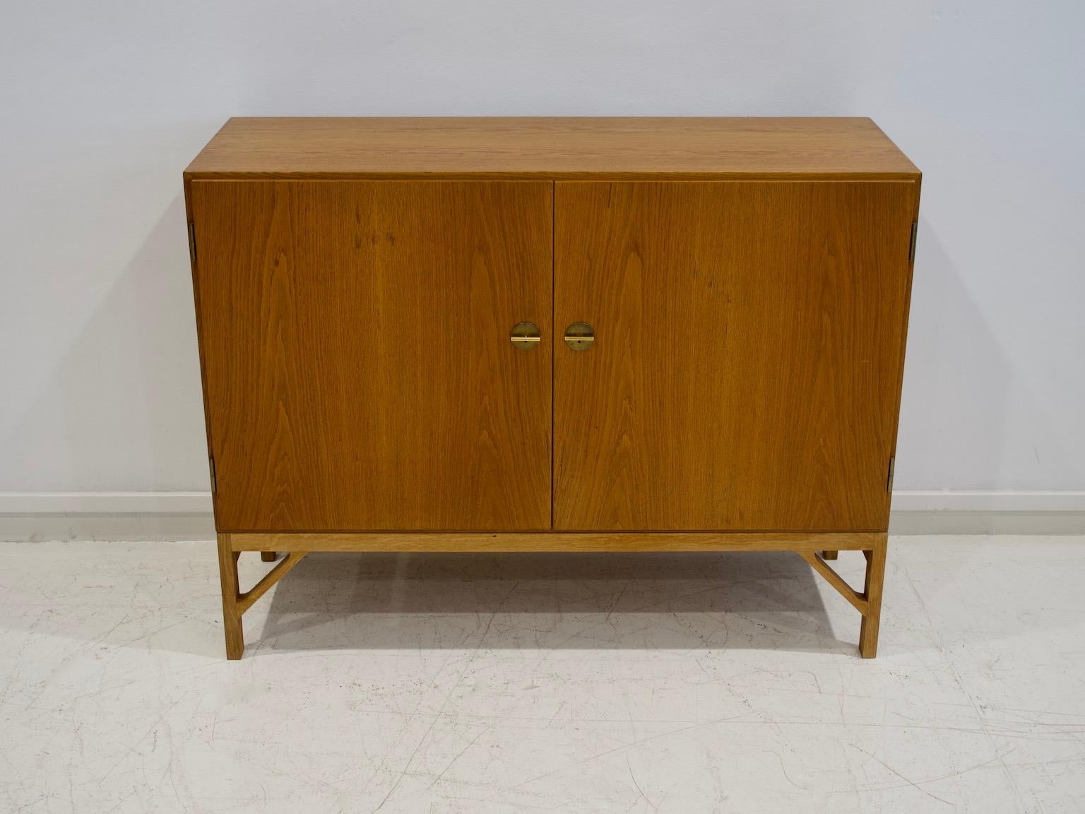 Oak cabinet, model 232, also known as 'China' cabinet, designed by Børge Mogensen and produced by FDB in Denmark. Mounted on later base. Front with two doors and brass keys that serve as handles. Inside with shelves and pullout trays. Manufactured