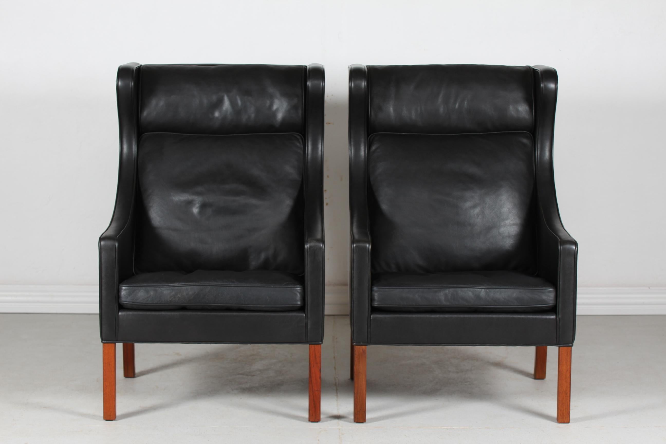 A pair of Danish vintage Børge Mogensen wingback chairs model no. 2204.
They are upholstered with the original black leather and the legs are made of solid walnut. 
The cushions are filled inside with granules and natural feathers which gives the