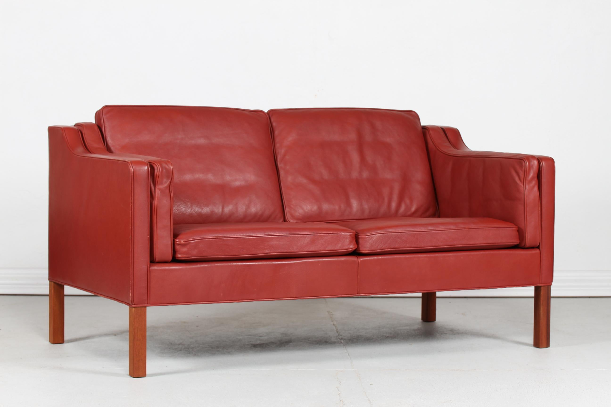 Danish vintage Børge Mogensen sofa for 2 persons model 2212.
It's upholstered with original brick red / red brown leather. The legs are made of mahogany. 
The cushions are filled inside with granules and natural feathers which gives the sofa a very