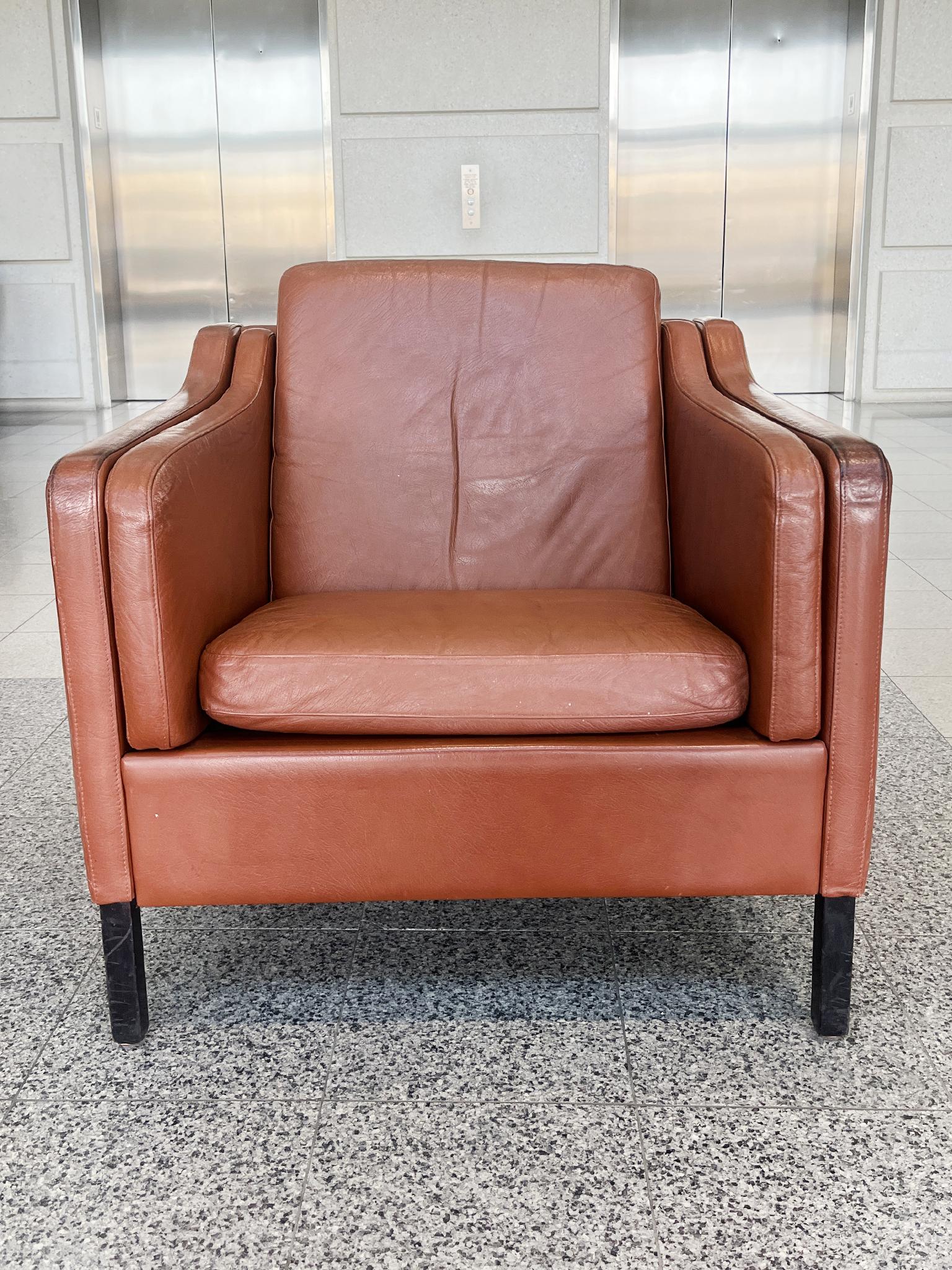 Fabricado en la década de 1970, este sillón moderno danés de cuero color caramelo fue diseñado al estilo de Børge Mogensen. Al igual que las sillas de Mogensen, este sillón presenta líneas suaves que se curvan y suavizan en las esquinas. Los amplios