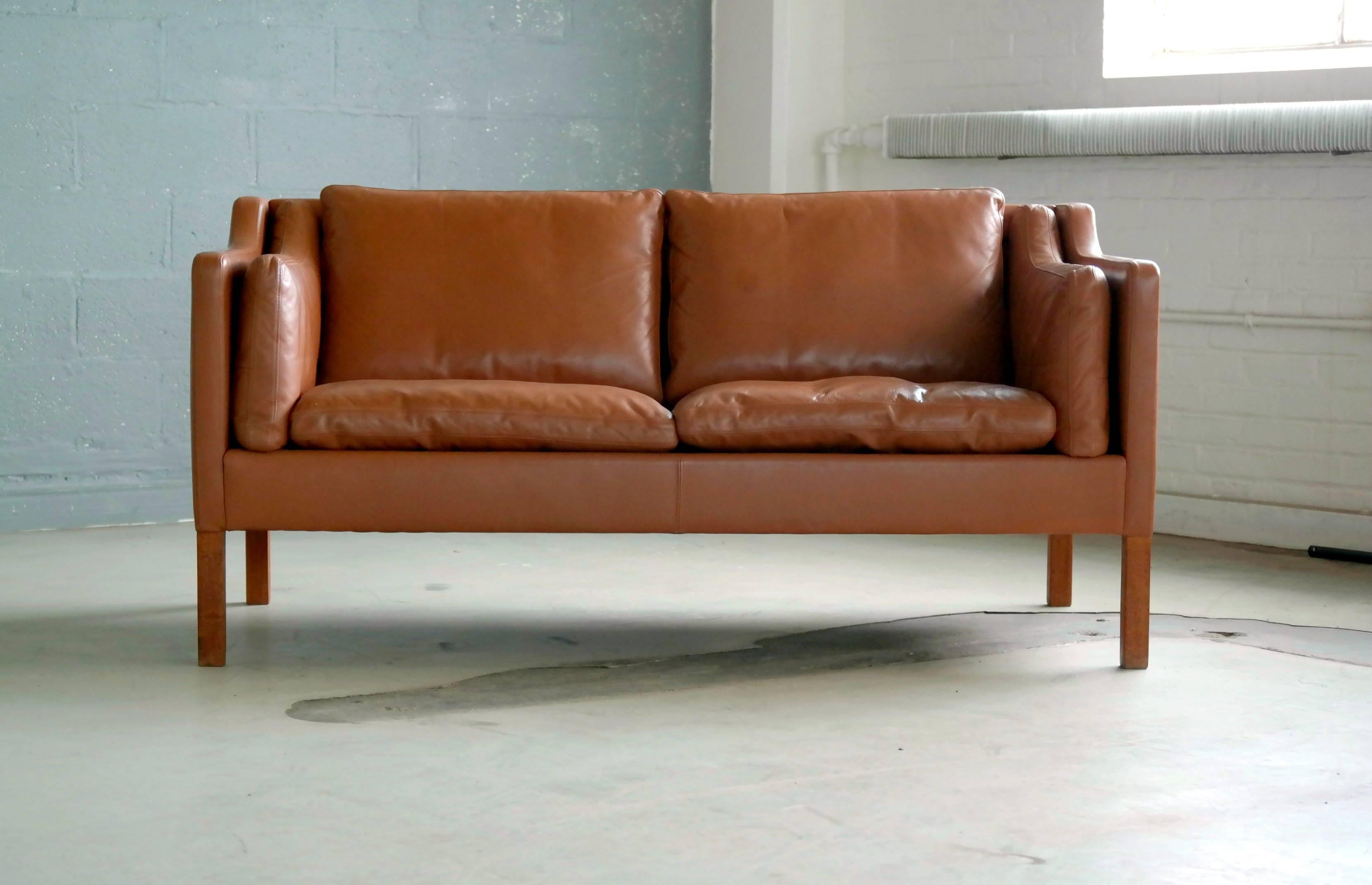 Classic two-seat sofa similar to Børge Mogensen's model 2212 in cognac leather with teak legs by Stouby Mobler, Denmark. One of the most classic, elegant and enduring designs coming out of Denmark in the midcentury era. Down filled cushions similar