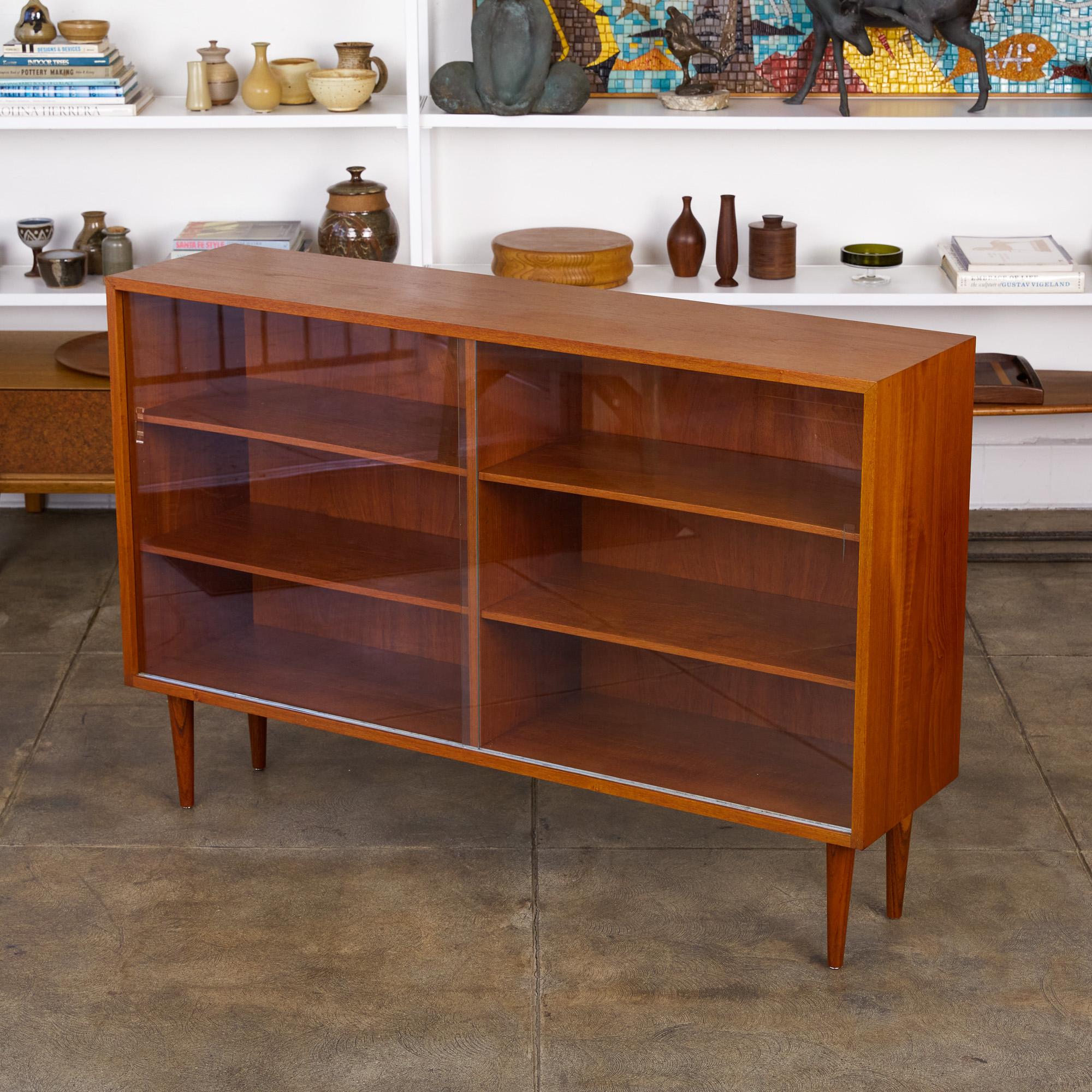 Børge Mogensen teak bookcase for Aalborg, Denmark, circa 1950s. The cabinet features a slender teak exterior frame and tapered turned legs. It has glass sliding door openings and four adjustable shelves.

Dimensions: 54.25” width x 13.5” depth x