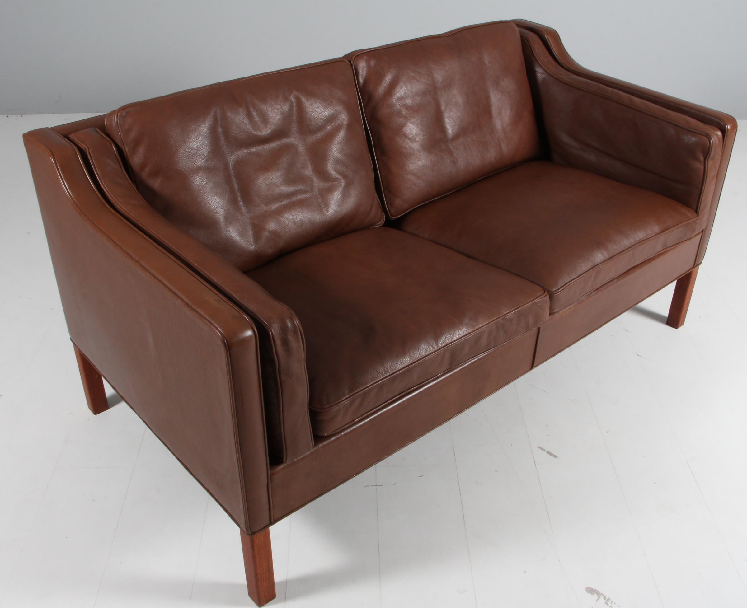Børge Mogensen two-seat sofa with original patinated brwon leather upholstery.

Legs of teak.

Model 2212, made by Fredericia Furniture.

Matching three seater, pair of lounge chairs and ottomans in stock.