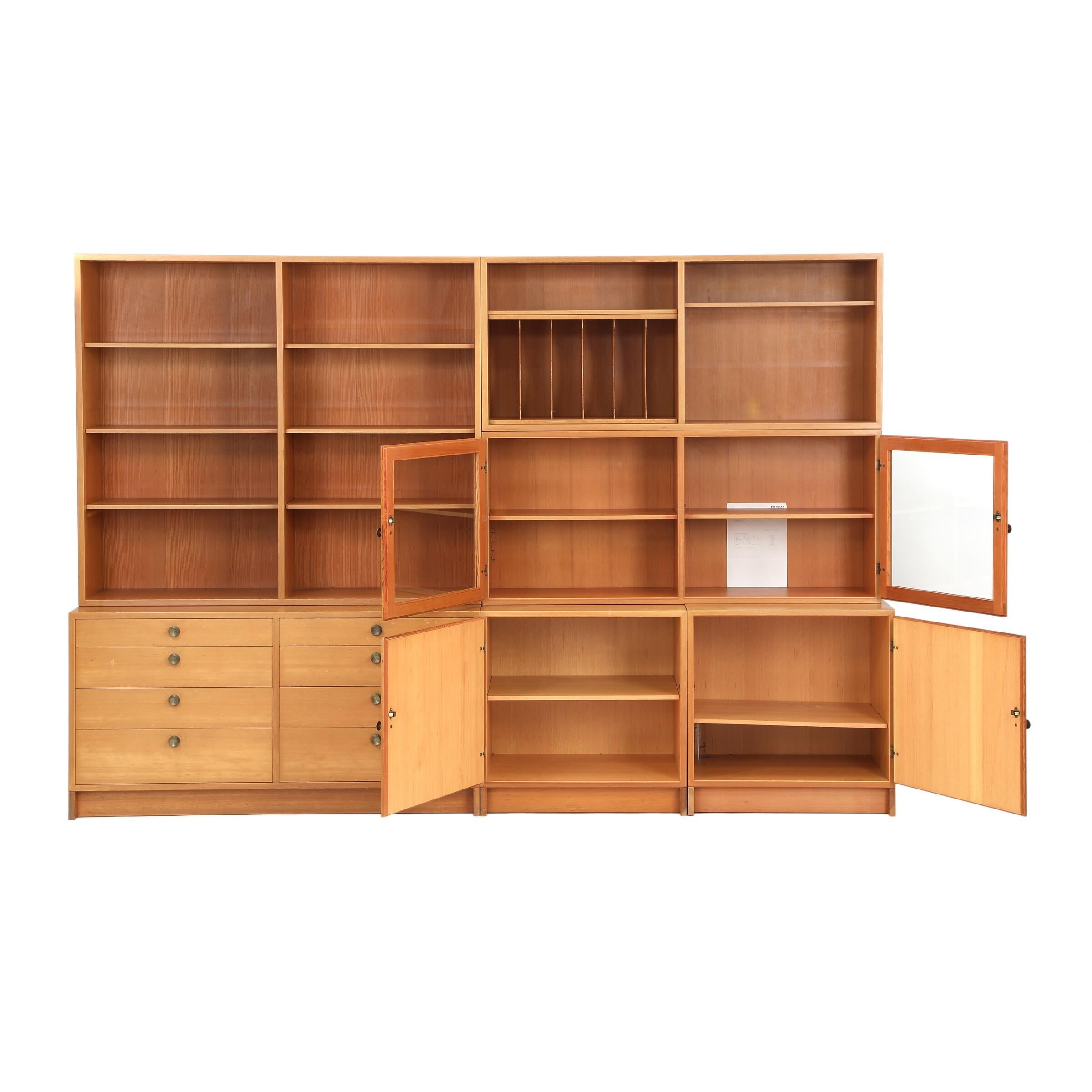 Wall unit of Oregon pine, consisting of three lower sections, hereof two with doors and one with drawers and three upper sections with show case and adjustable shelves. Handles and fitting of brass. Manufactured by Karl Andersson & Söner,