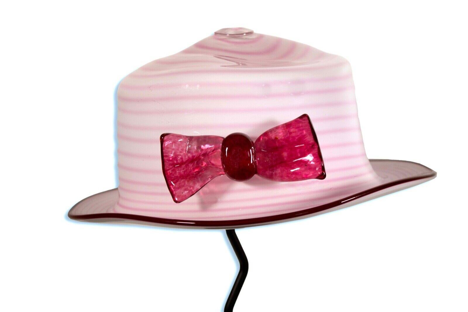 A lovely studio art blown glass sculpture depicting a life size pink hat on a display stand by Brian Brenno. Etched signature on brim. Circa 1990s. The design features a classic brimmed hat with a striped design and pink bow. Adds an element of
