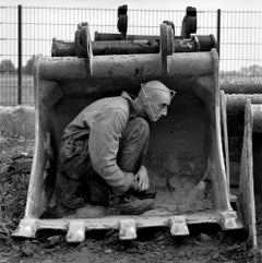 A portrait of working man hiding in the digger with metal pyramid on his head