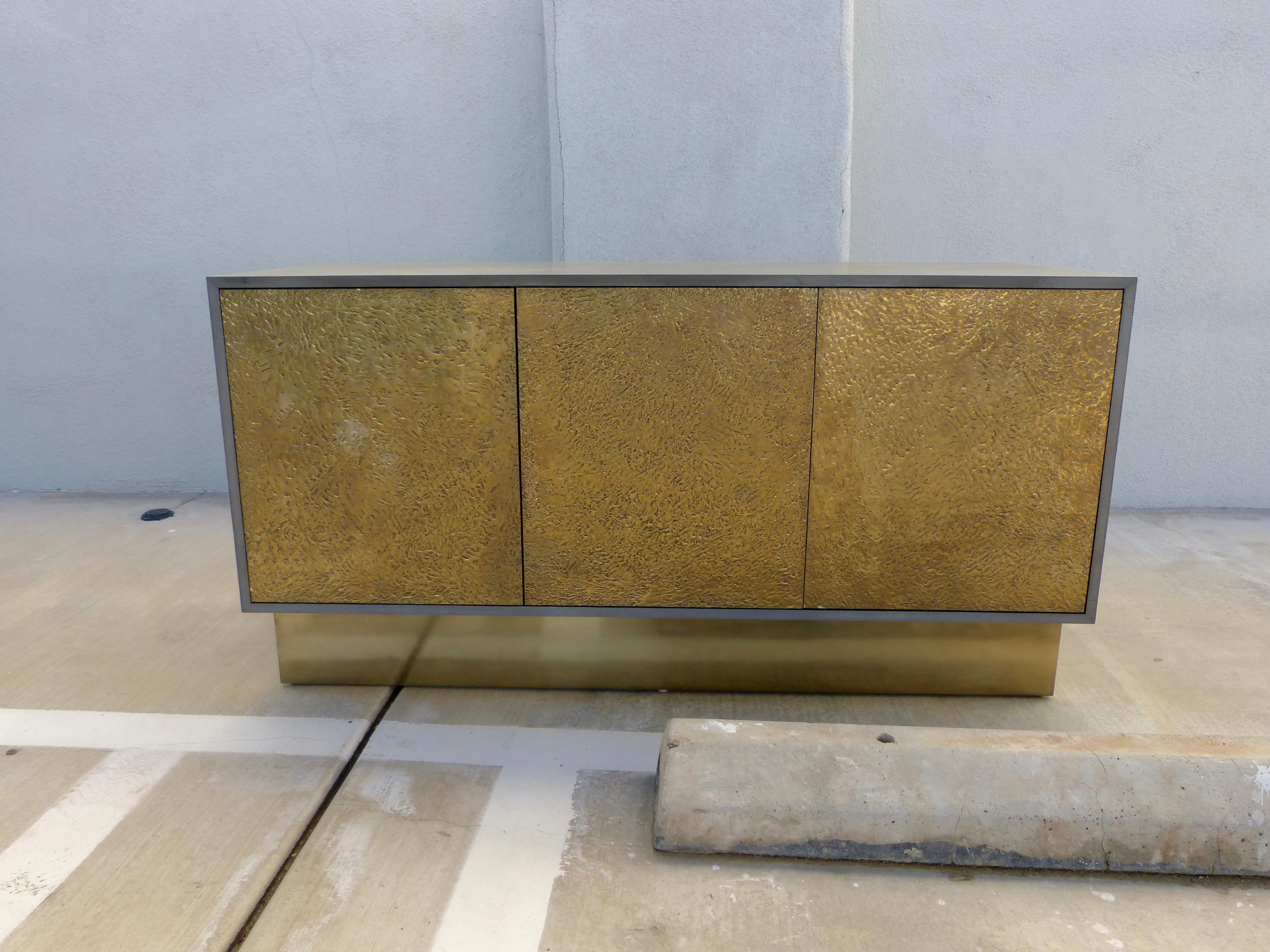 A beautiful bridges over time originals custom made credenza.  It is coated in an iron coating and a brass abstract front. Each section has one shelf. The iron finish has been acid washed to give it a worn 