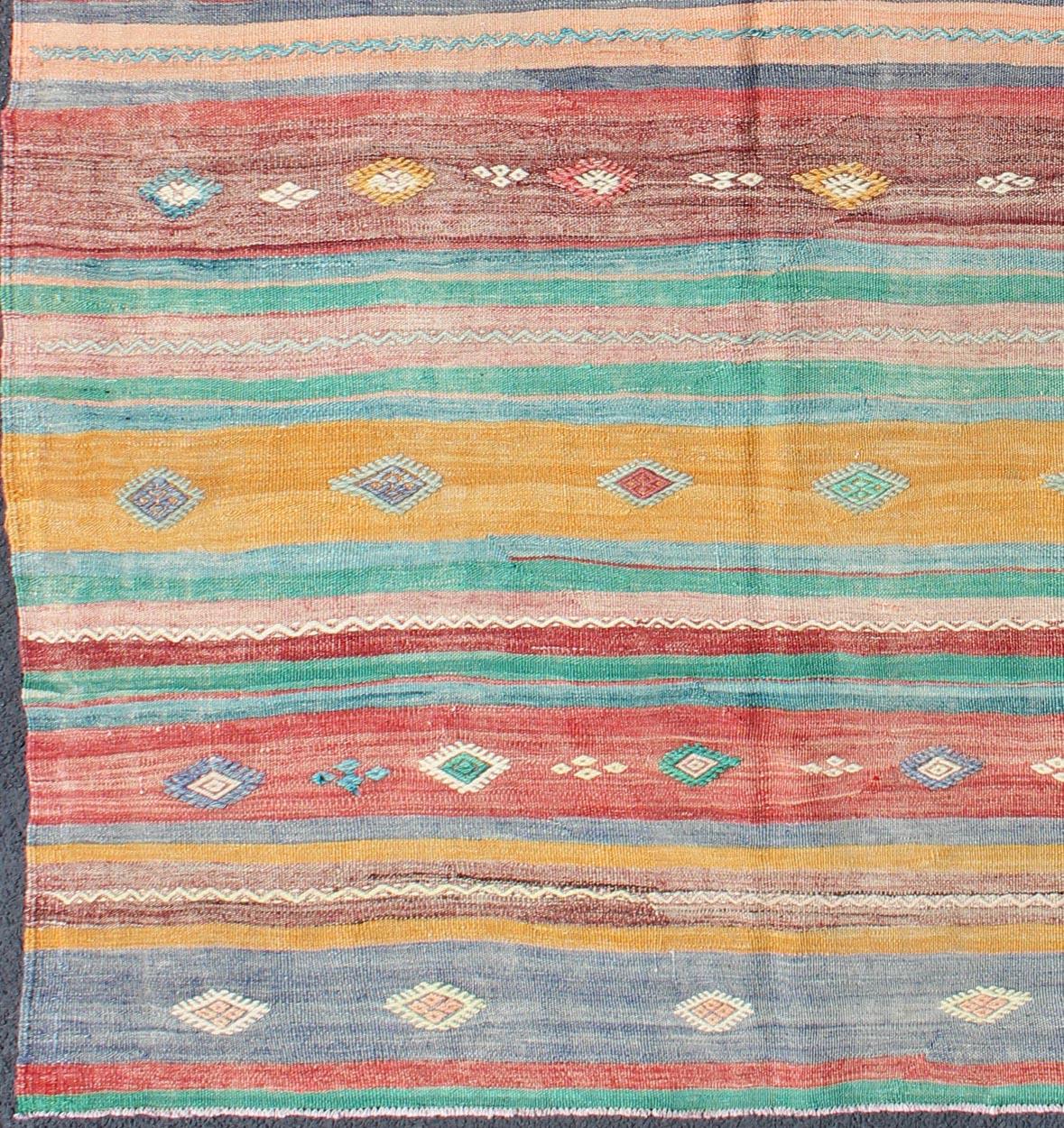 Featuring geometric tribal shapes rendered in a repeating horizontal stripe design, this unique midcentury Kilim showcases an array of bright and cheerful colors, including teal, blue, golden yellow, red, salmon pink, and ivory.

Measures: 5'4'' x