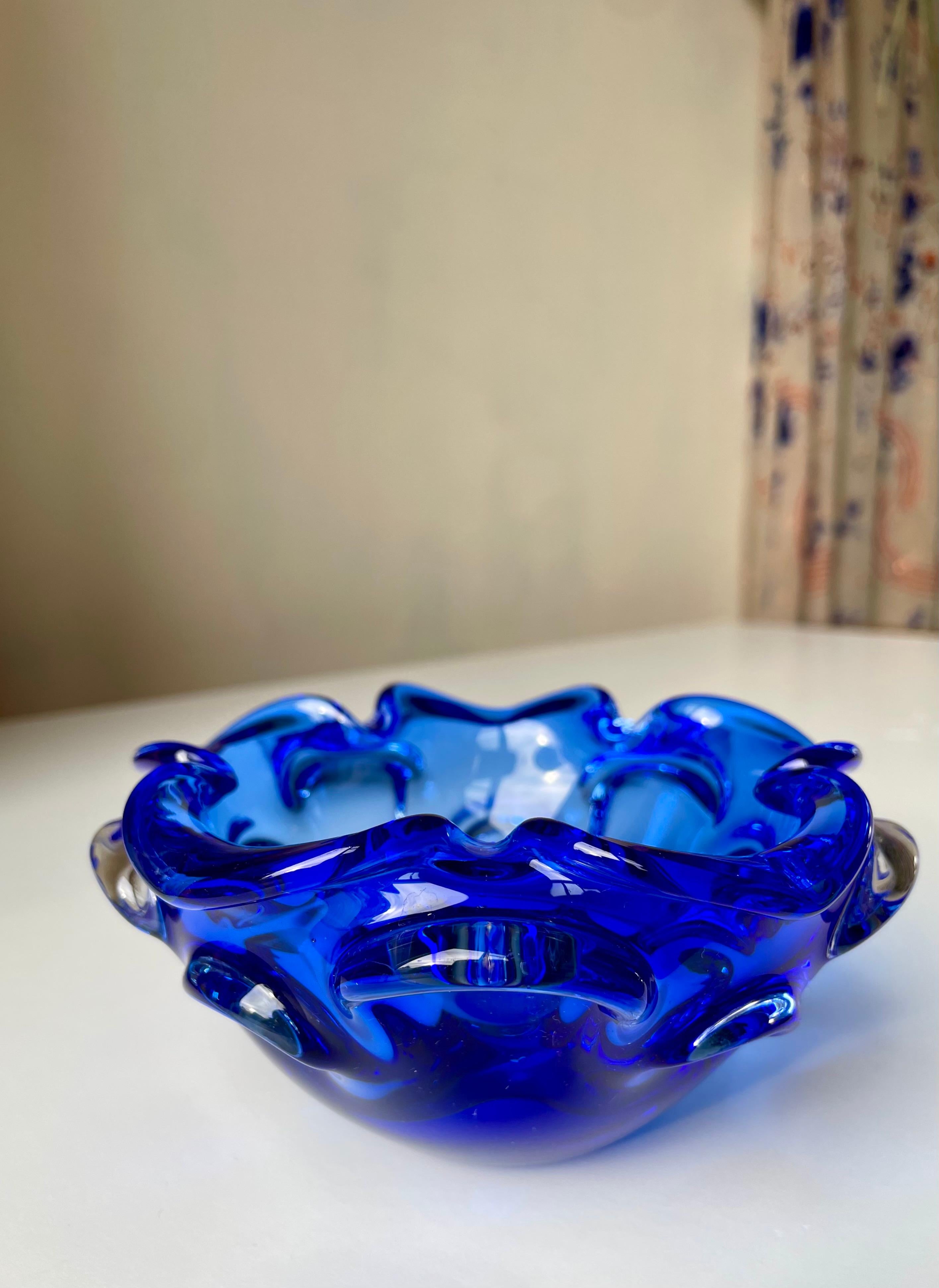 Mouth blown Swedish modern encased vivid blue art glass bowl in Murano Sommerso style. Round shape with large frills around the edge and multiple symmetrical waves decorating the exterior of the bowl. A heavy, solid decorative glass piece in