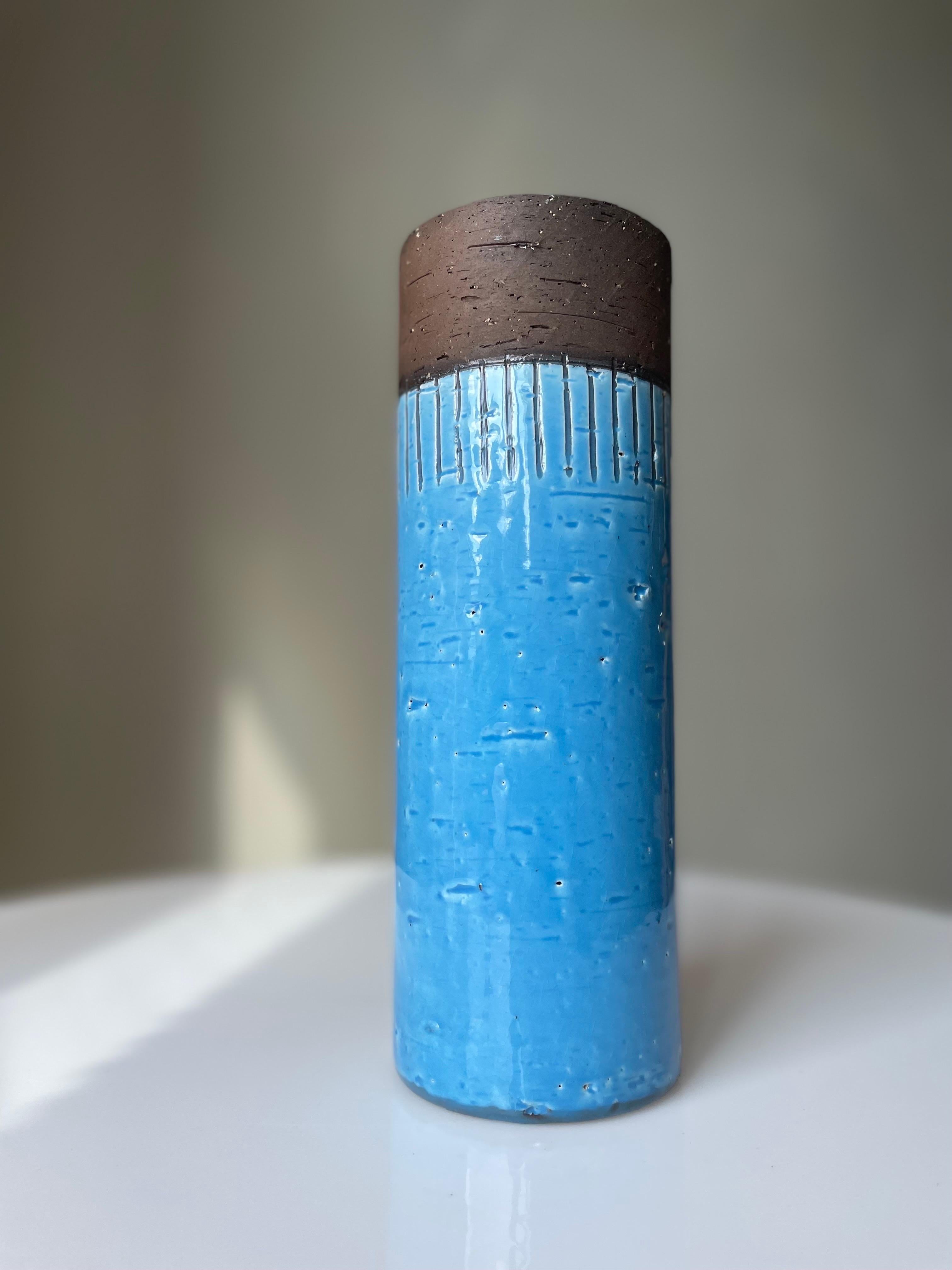 Tall handmade cylinder shaped Swedish midcentury modern ceramic vase with bright blue glaze on the outside and clear glaze on the inside. Top part left unglazed and right below are handcarved relief lines toward the shiny blue glaze. Manufactured by