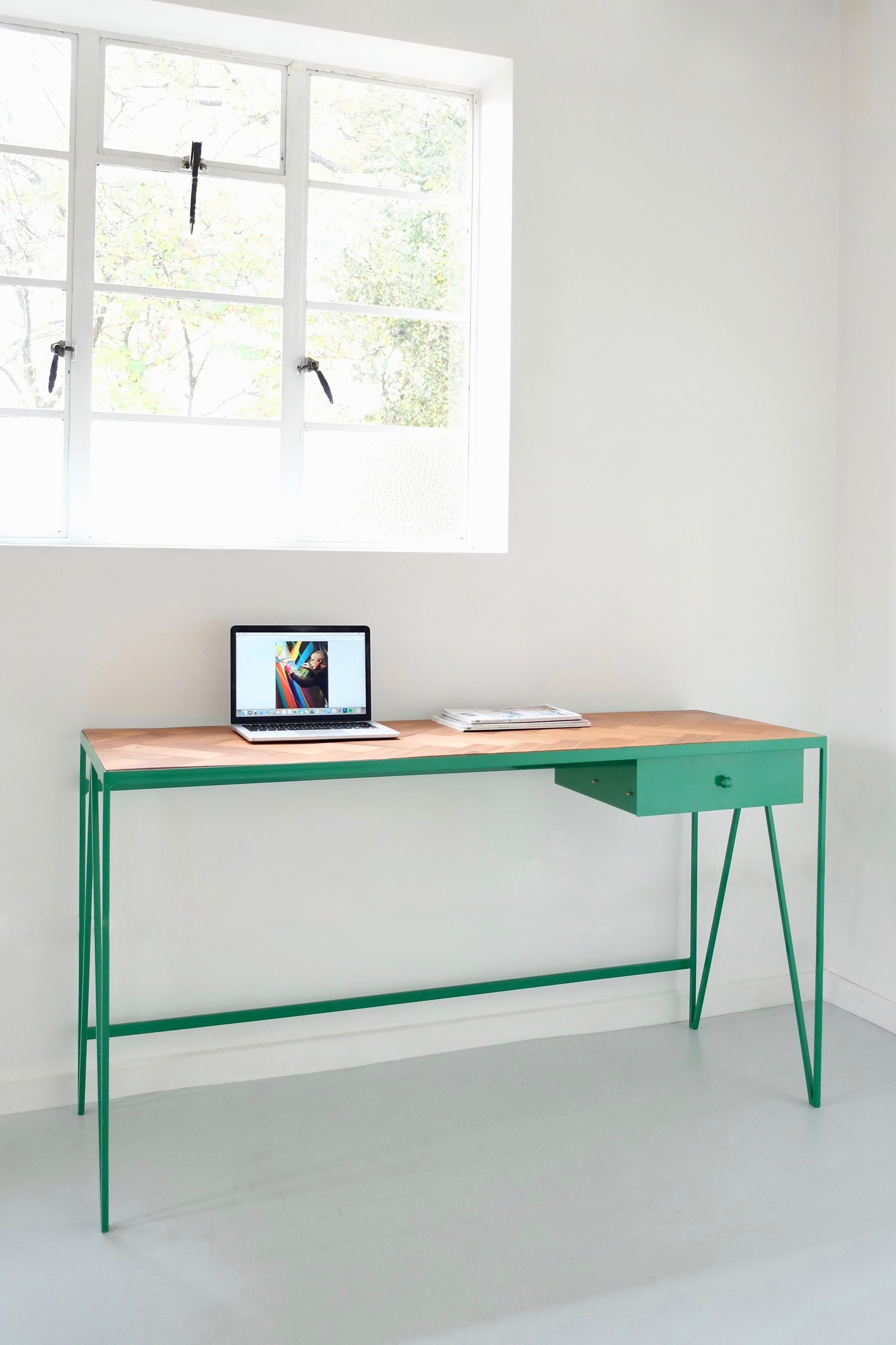 The Study desk is made with a green powder coated steel frame and a beautiful parquet wood table top. This minimal desk has a steel drawer suspended underneath the table top with a loop handle. The parquet wood table top is handmade from reclaimed