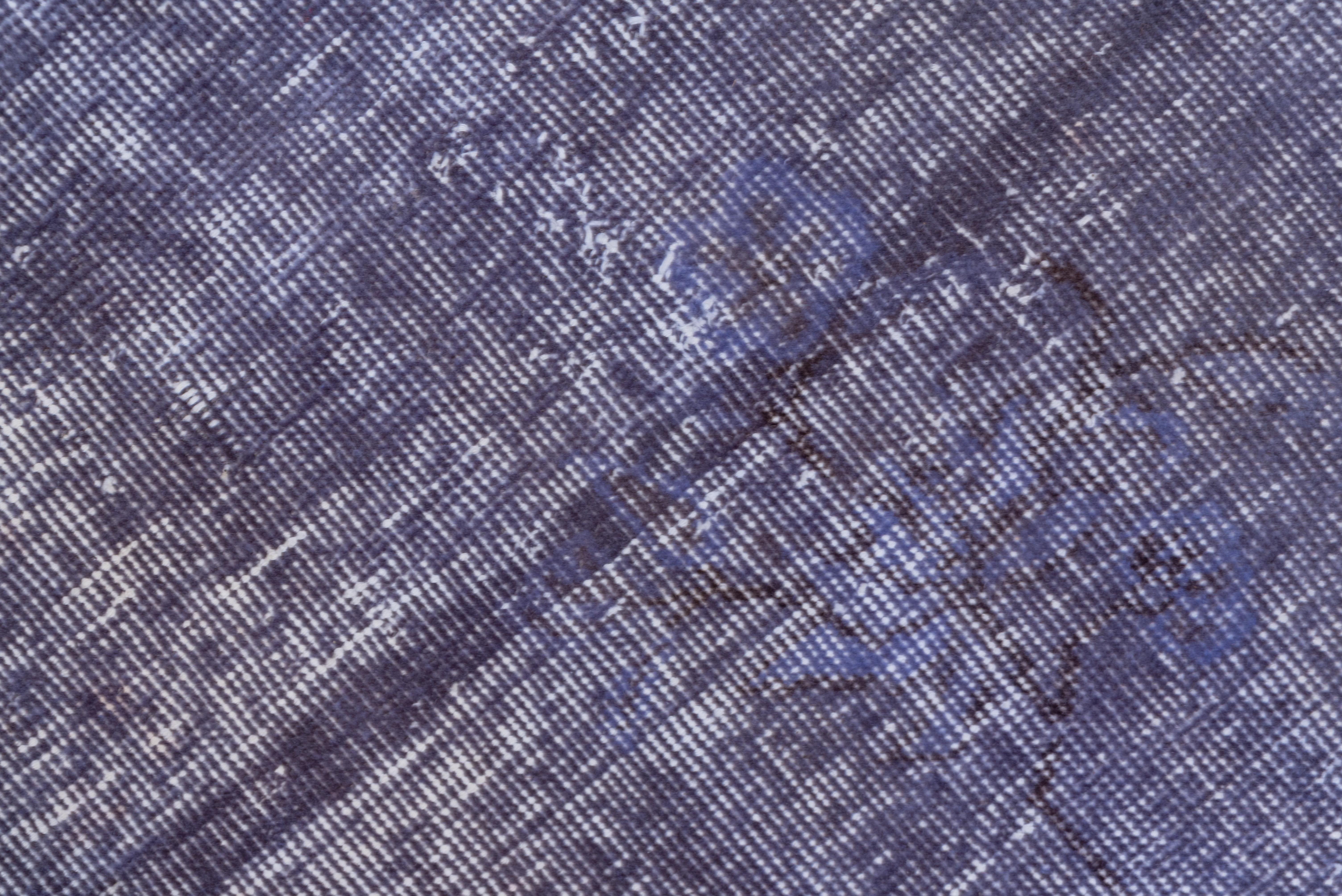 This light purple rather distressed overdye carpet shows a border of scrolling tendrils framing barely visible lobed medallion. The off white foundation adds another overall secondary tone to the purple and dark brown.