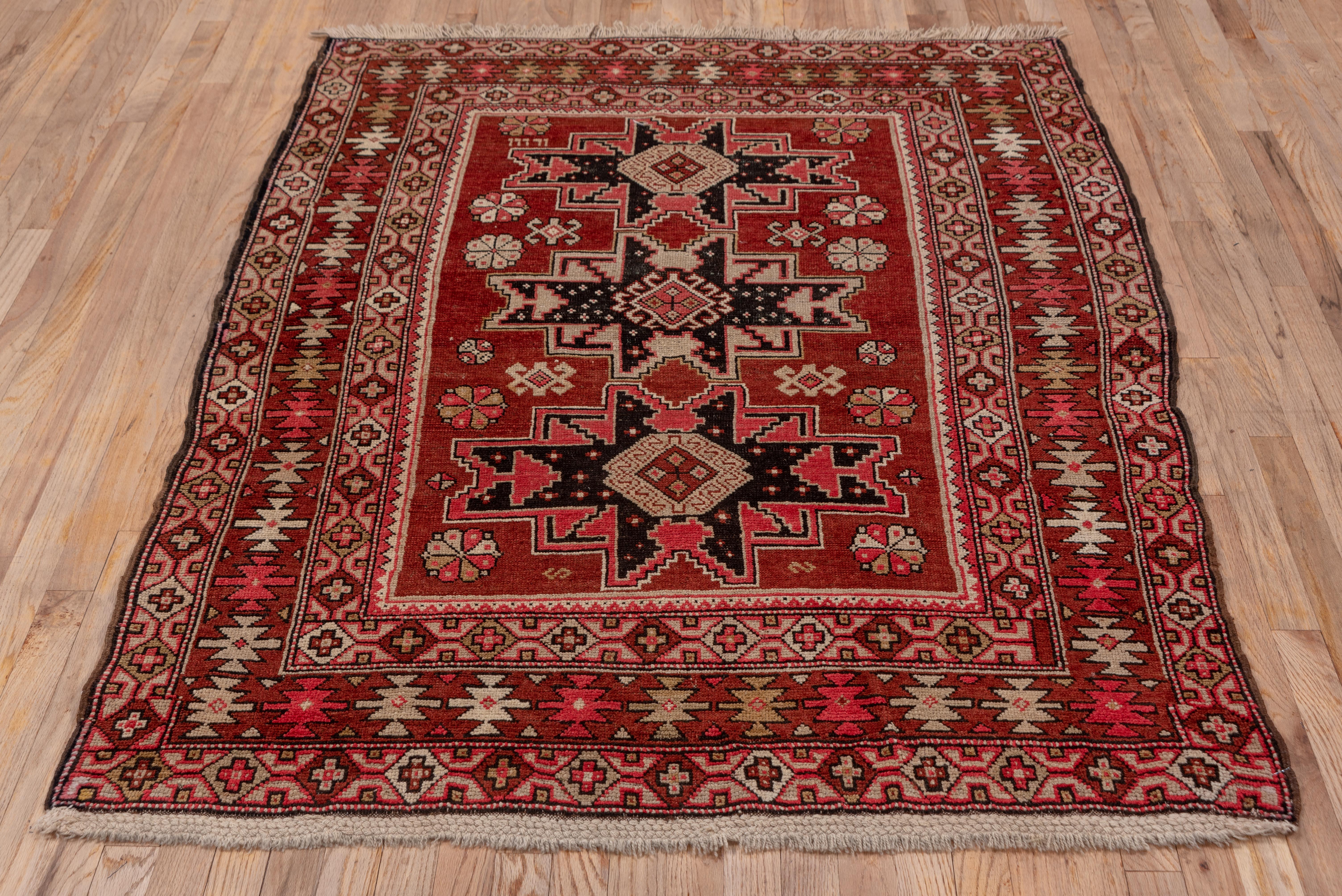 The ruby red field displays three Lesghi stars in cream and navy, supported by a scatter of rosettes and hooked lozenges. The red main border shows disjoint ashiks on this Classic east Caucasian fine-weave scatter.