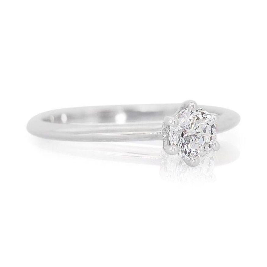 Dieser Ring ist nicht nur ein Schmuckstück, er ist eine Einladung, den Glanz des Lebens zu umarmen, wobei jede Facette Freude und dauerhafte Schönheit verspricht. Sein Herzstück, eingebettet in 18 Karat Weißgold, ist ein prächtiger runder Brillant