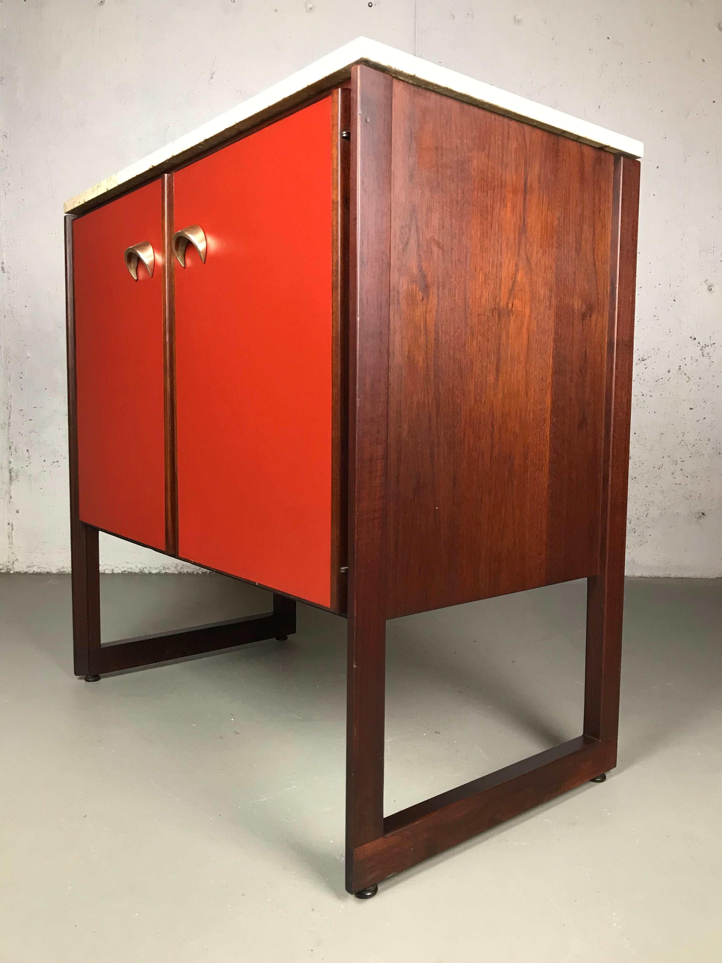 Wonderful example of American Modernism by Jens Risom. This cabinet is made of a wonderful use of contrasting materials: walnut, rosewood, travertine marble, red vinyl and brass. Rosewood is used in the trim around the doors, framing pieces and