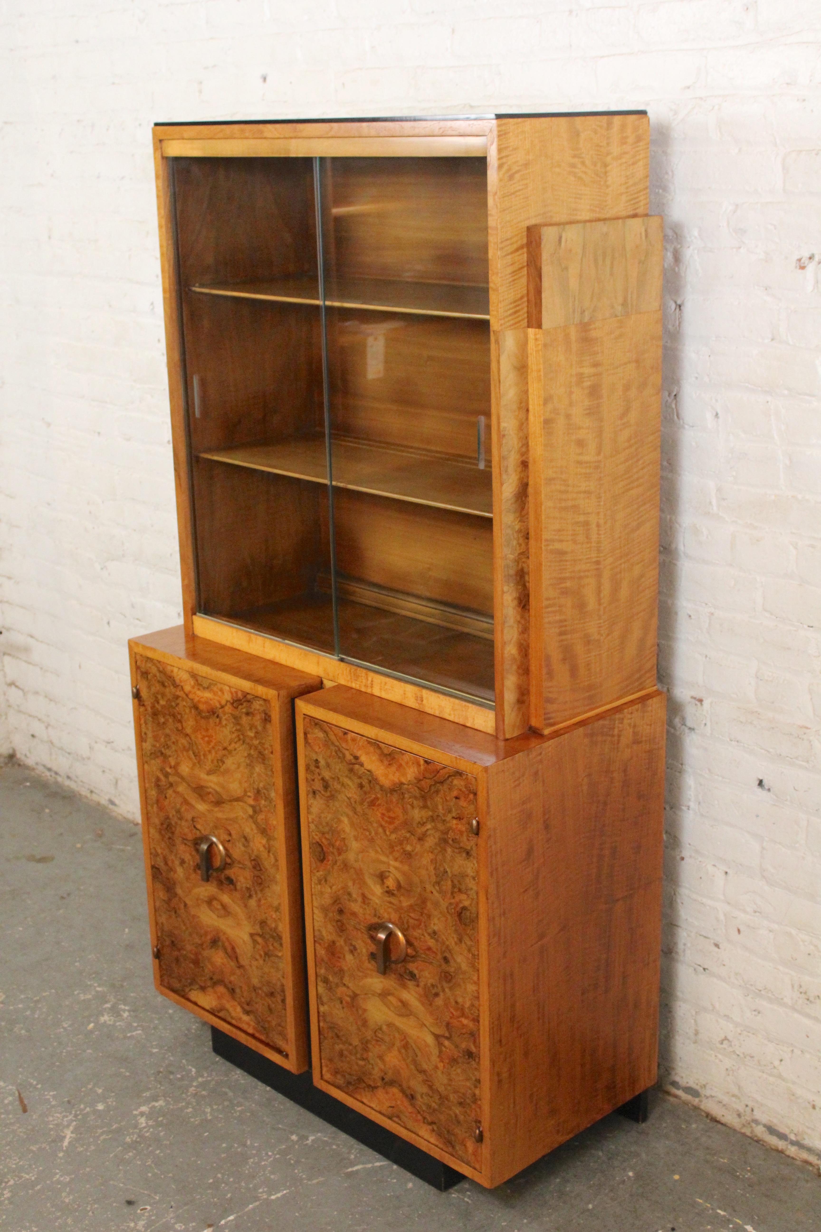 This display cabinet is made of burled maple with black accents and brass hardware. Two sliding glass doors cover open display storage, two burl front doors cover the bottom cabinet storage. Great for displaying your glassware or
