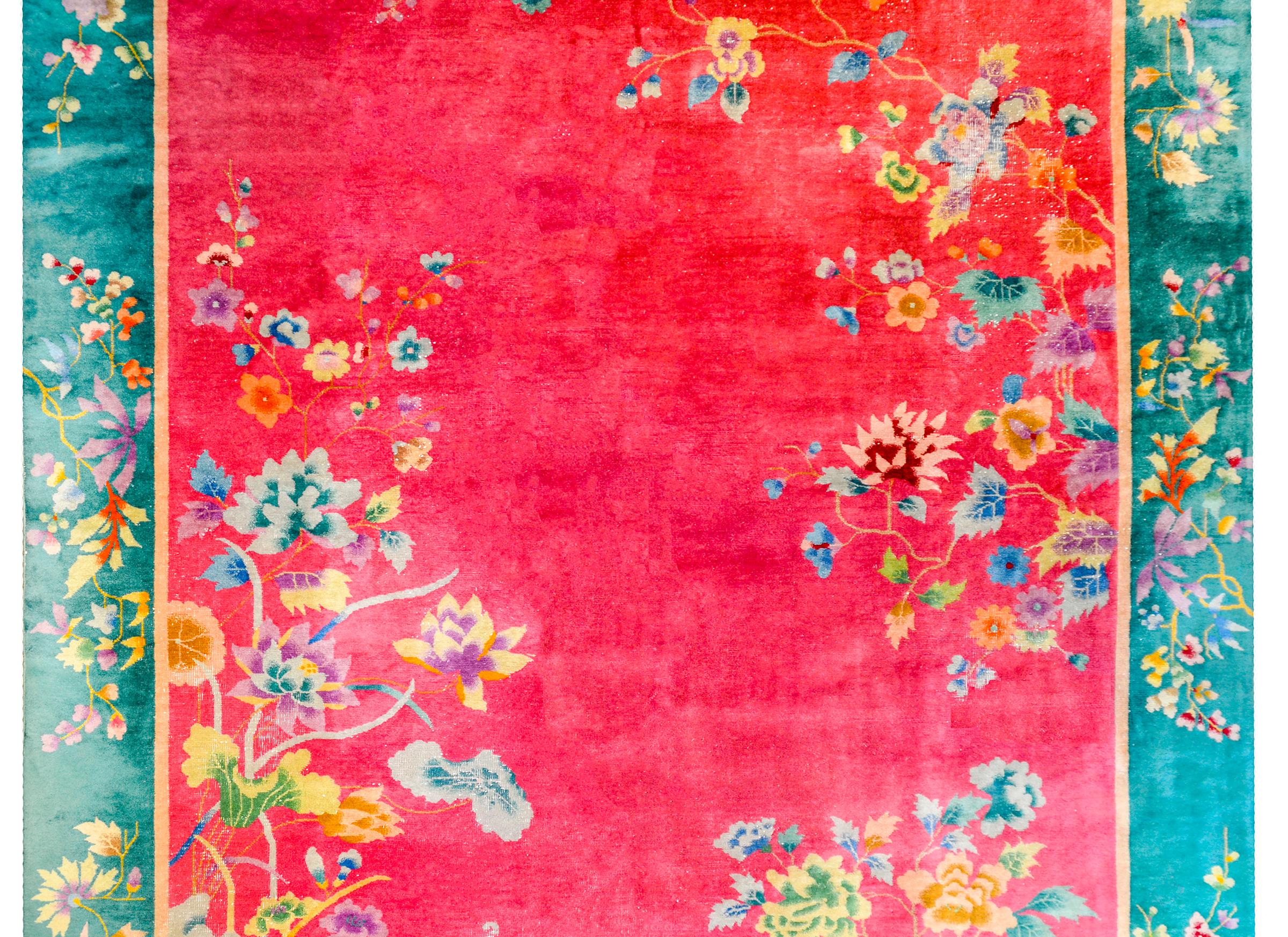 A brilliant early 20th century Chinese Art Deco rug with a bright fuchsia field with a scholar's rock in the lower left corner with multicolored lotus blossoms and large leaves, a potted tree peony in the lower right corner, and a blossoming prunus
