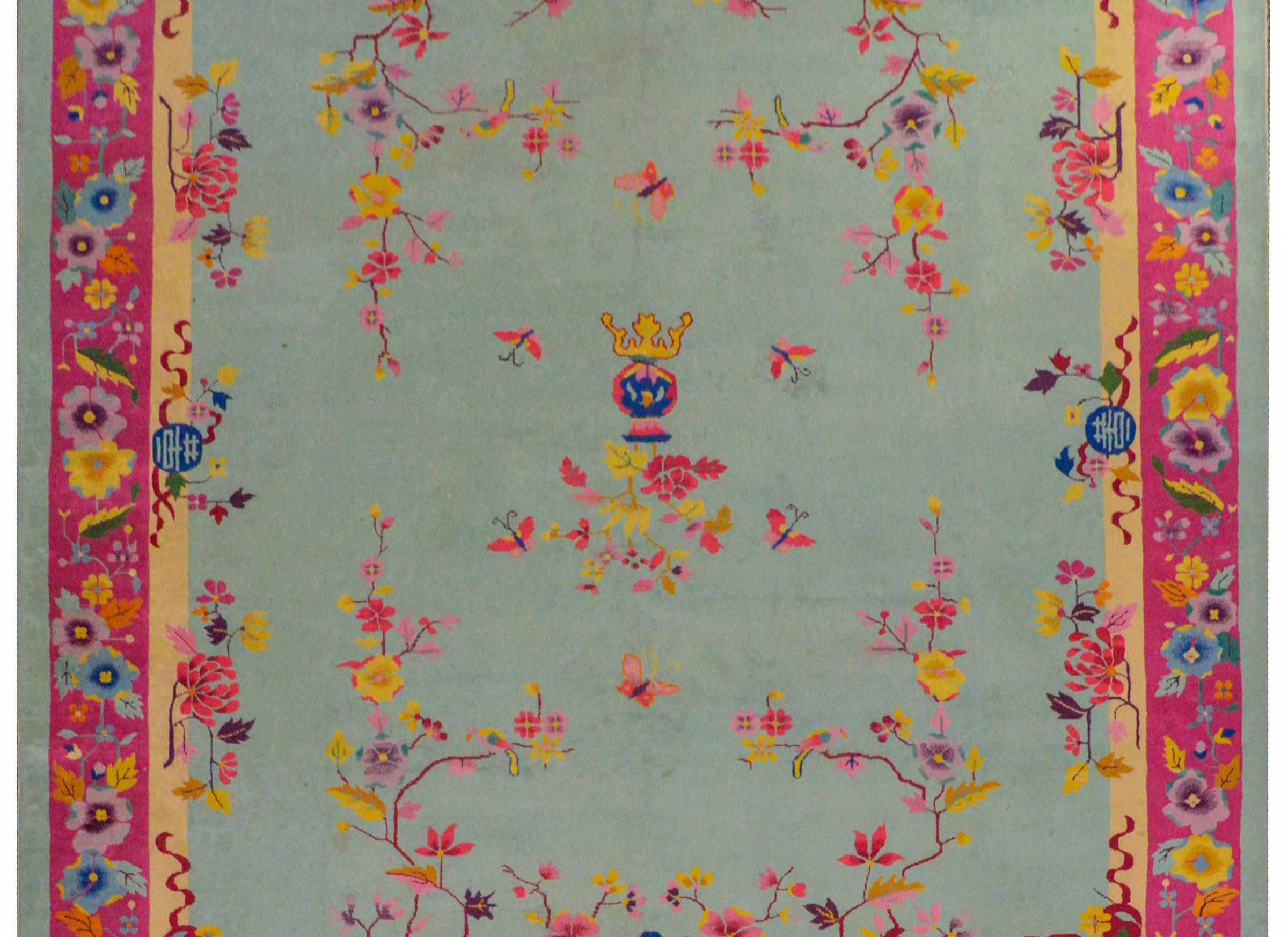 A brilliant Chinese Art Deco rug with an unusual color palette of pinks, fuchsia, gold, orange, and lavender on a pale indigo background surrounded by a border of myriad flowers and leaves woven in bright colors.