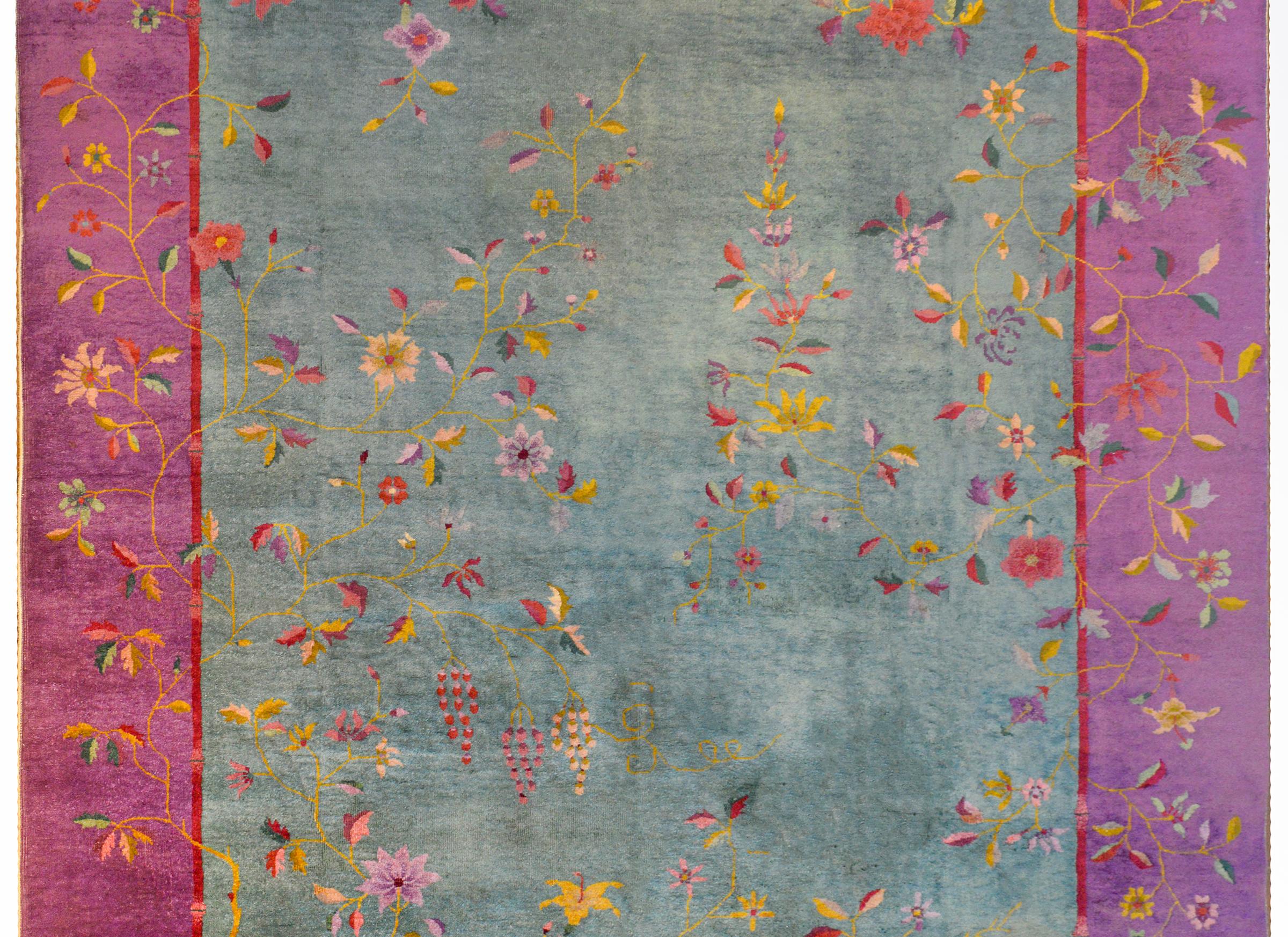 A brilliant early 20th century Chinese Art Deco rug with a pale mint green field surrounded by a wide fuchsia border with a thin crimson inner stripe. Myriad flowering branches and vines including chrysanthemums, peonies, and sherry blossoms overlay