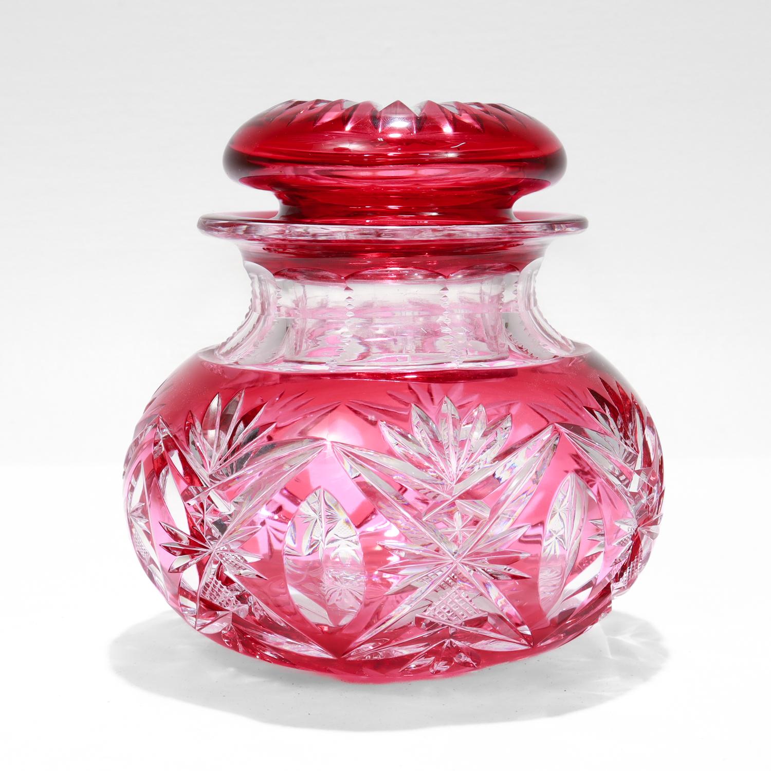 A fine vintage cut-to-clear glass jar. 

In cranberry cut-to-clear glass.  

Attributed to the Val Saint Lambert glass company.

In a rare, covered jar form in (an apparently unnamed, but numbered) pattern 3247 / 17. 

The sides feature a repeating