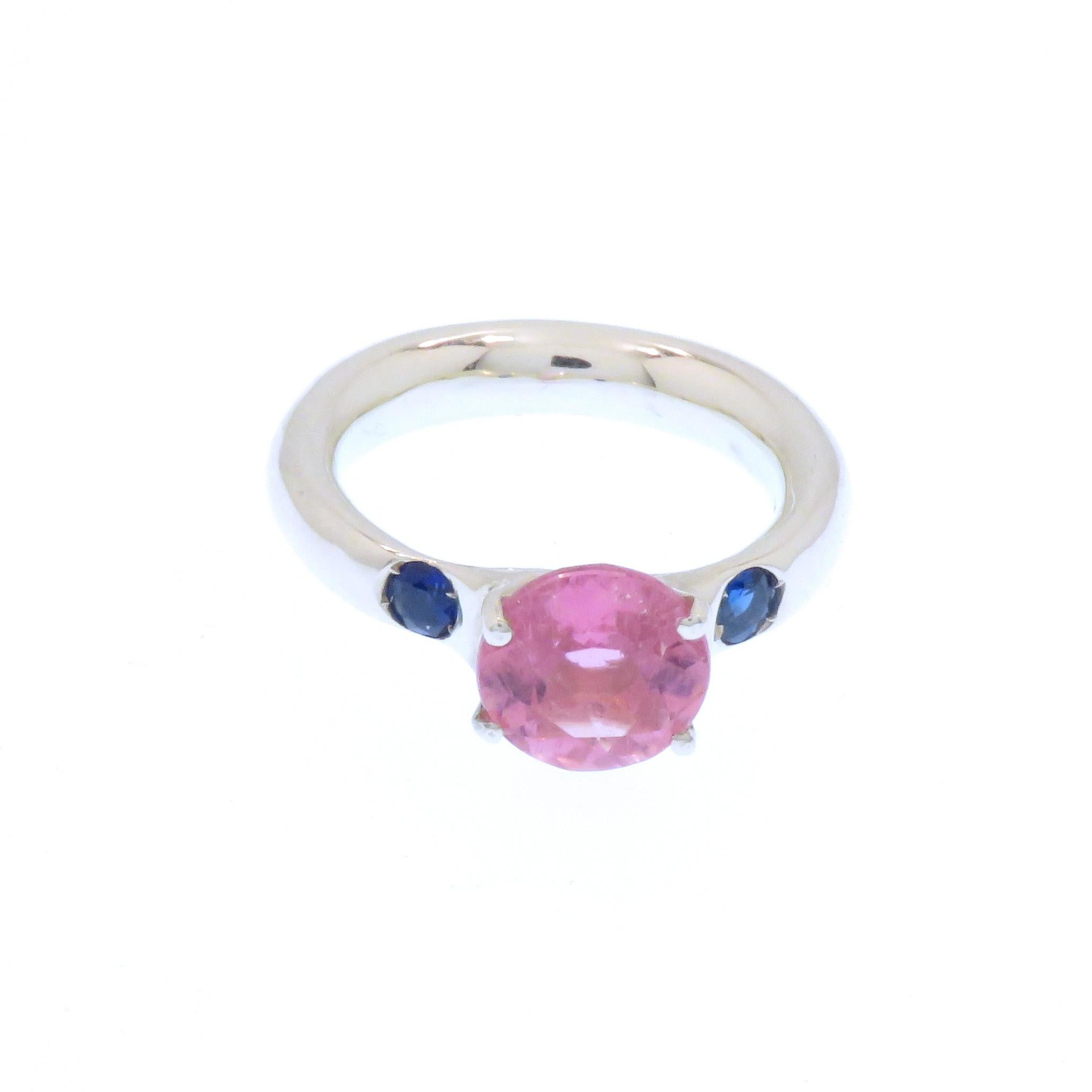 Elegant ring crafted in 9k white gold featuring a natural 2.25 ctw brilliant cut pink tourmaline  in its centre, flanked by two round cut blue sapphires weighing 0.25 ctw, The dimension of the tourmaline is 8.40 millimeters / 0.330 inches. Us finger