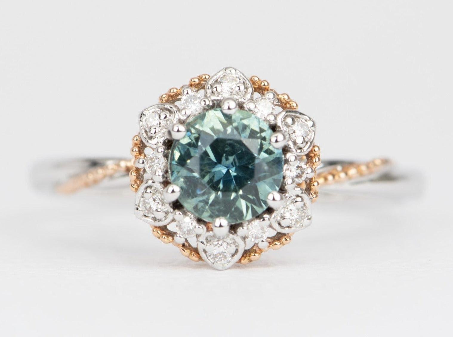 A beautiful teal blue Montana sapphire in the center, adds a pop of color and individuality to the piece, making it a special choice for an engagement ring. The floral style of the ring adds a touch of elegance and femininity, making it a perfect