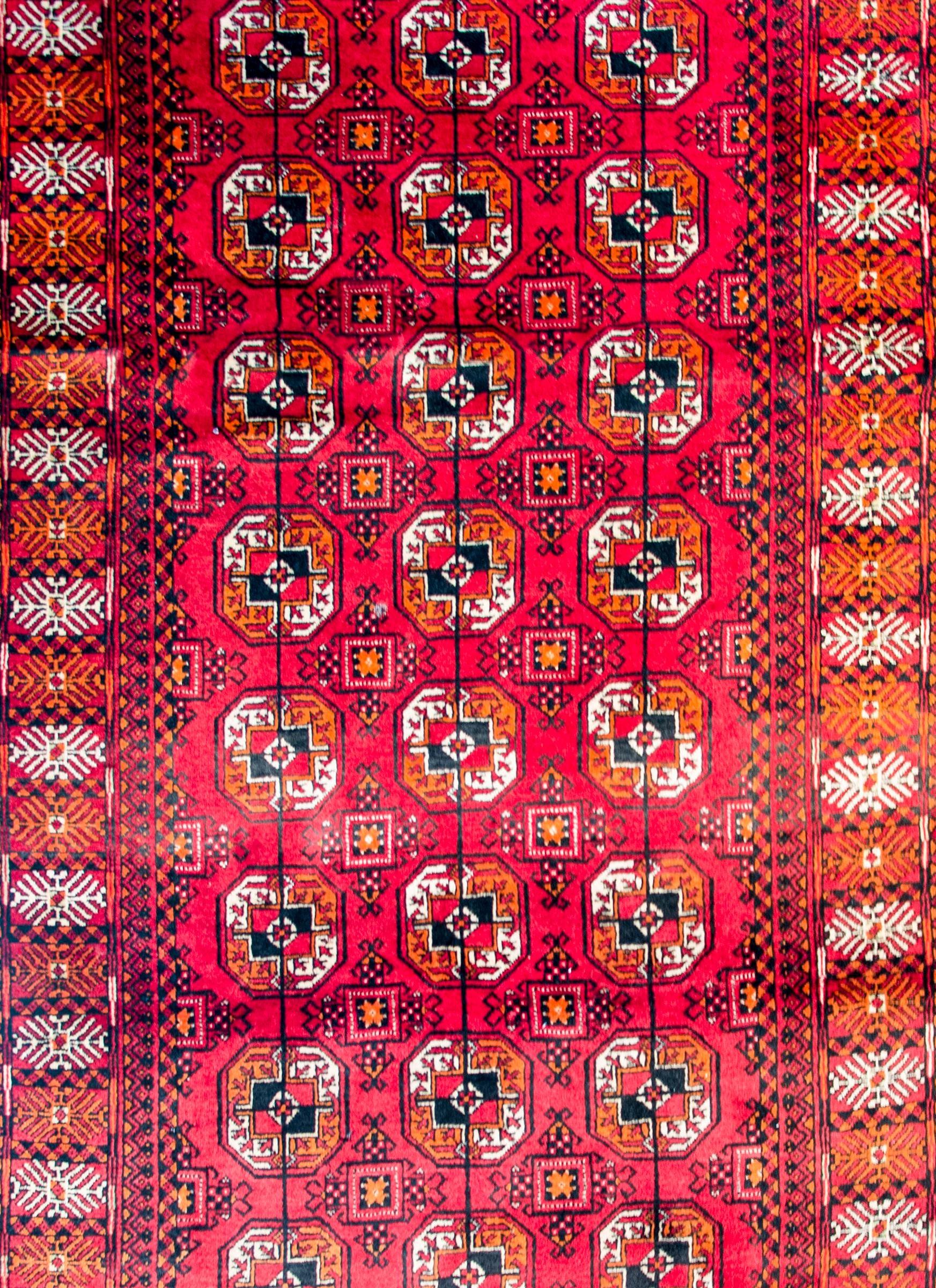 Un brillant tapis pakistanais vintage Bokhara avec un motif de médaillons en forme de losange en laine cramoisie, indigo et blanche sur un fond cramoisi foncé. La bordure est large et comporte un grand motif floral géométrique stylisé complémentaire.