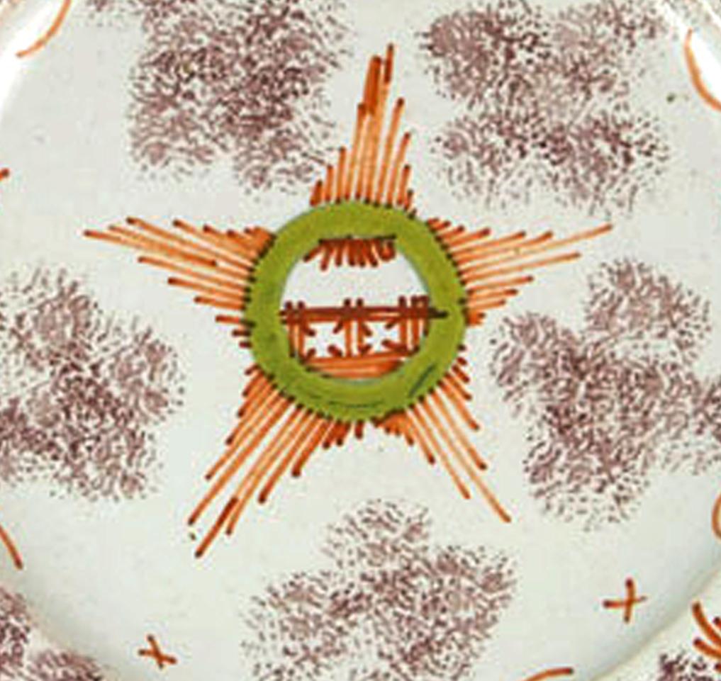 The Bristol delftware plate has a charming whimsical design with sponged manganese and a central star design containing a chinoiserie fence.

 