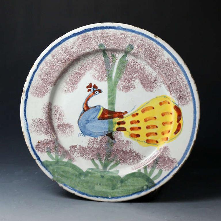 A highly decorative delftware polychrome plate decorated with a peacock perched somewhat comically in a tree. The naive rendition is exceptional and very full with very strong application of the colors especially the yellow tail of the bird.
