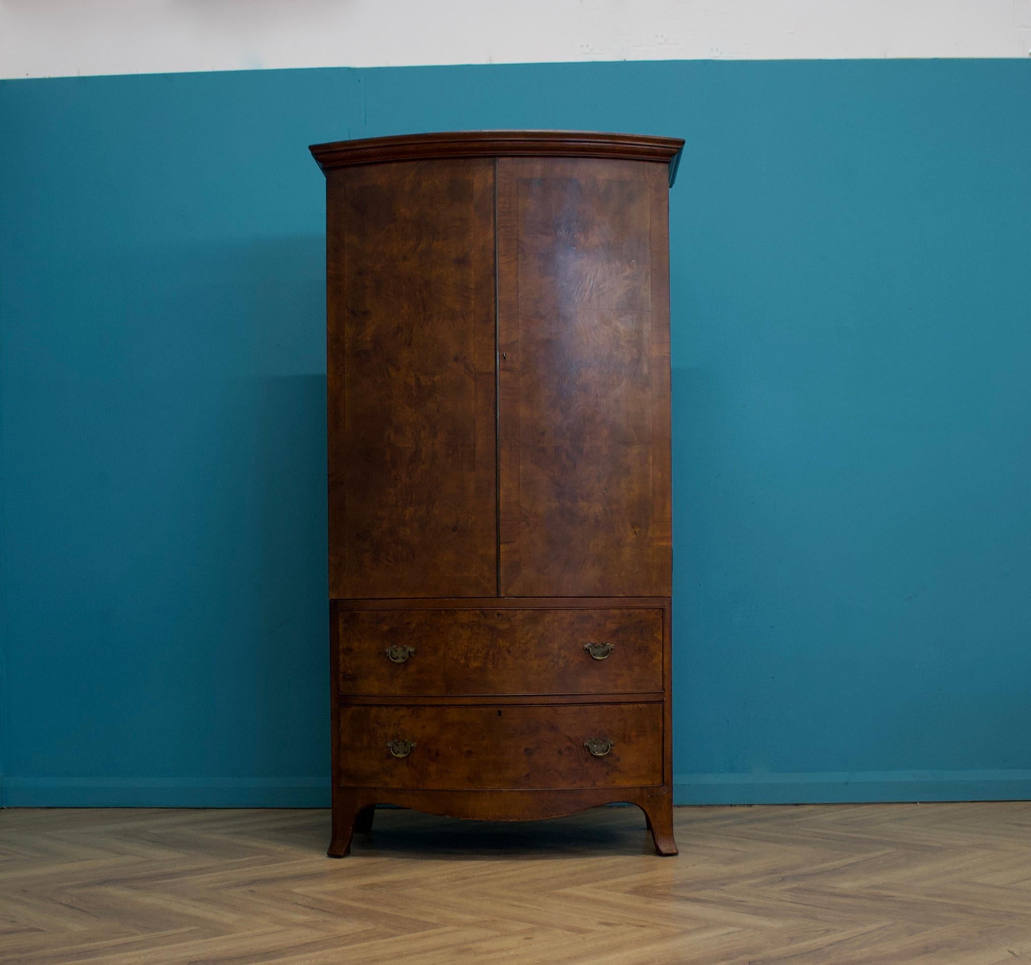 An impressive quality, 1930's burr bow fronted solid oak and walnut veneered wardrobe in the George III Style

The interior is fitted with a hanging rail, coat hooks and a recess which sits behind a dummy drawer

There is a functional drawer to the