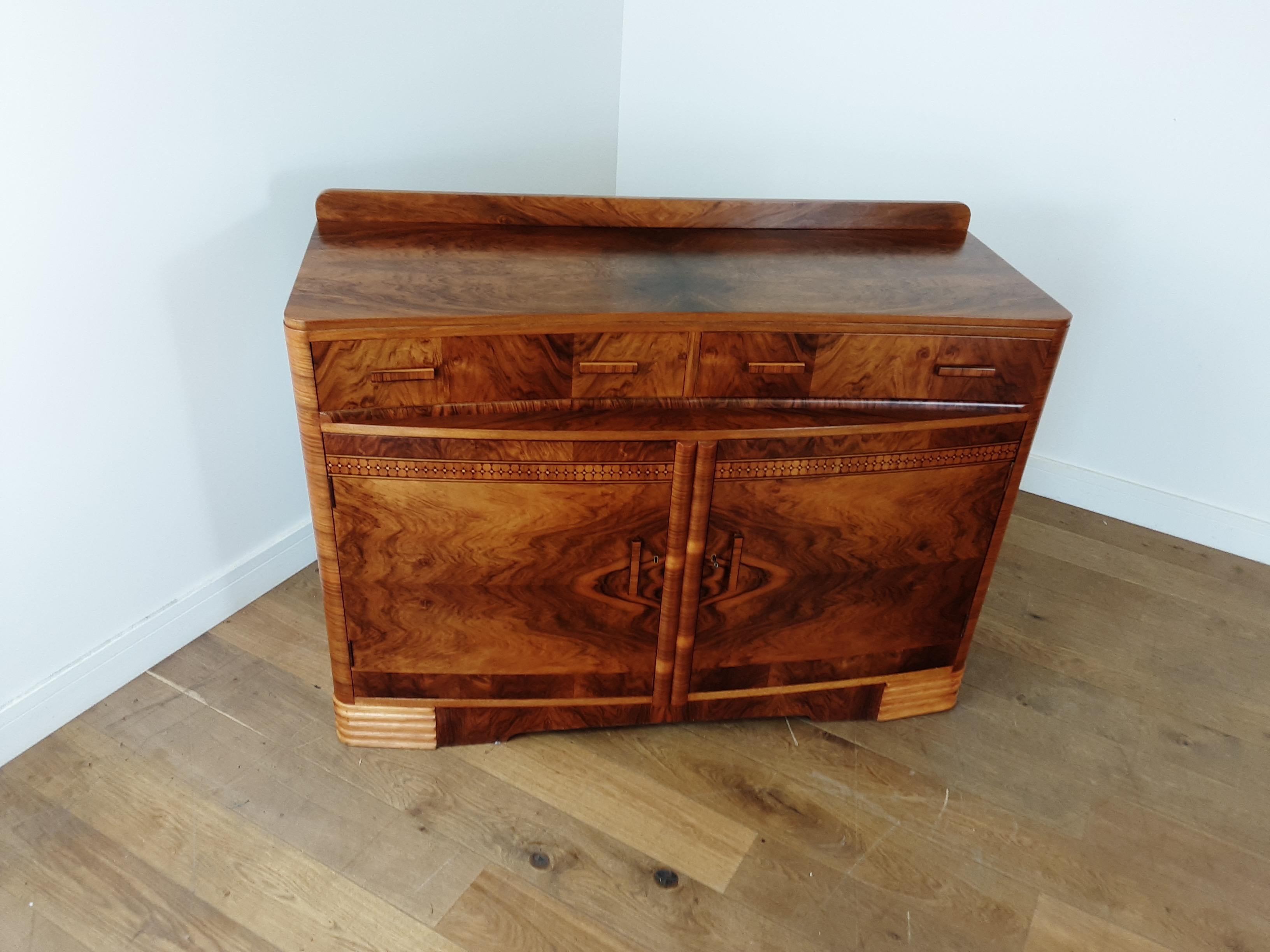 Art Deco sideboard.
Utterly beautiful, this sideboard has a stunning figured walnut with a beautiful marquetry band, the two drawers sweep in to meet giving a curved ledge, the edges are all rounded off, contrasting veneer to the base showing