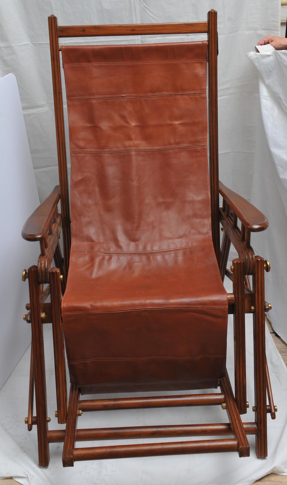 From the early 1900s, a British Campaign safari chair with cognac leather seat. It folds, it reclines and has a canvas option to switch out for cooler weather, which is included. A simple dowel above and below holds the fabric in place and can