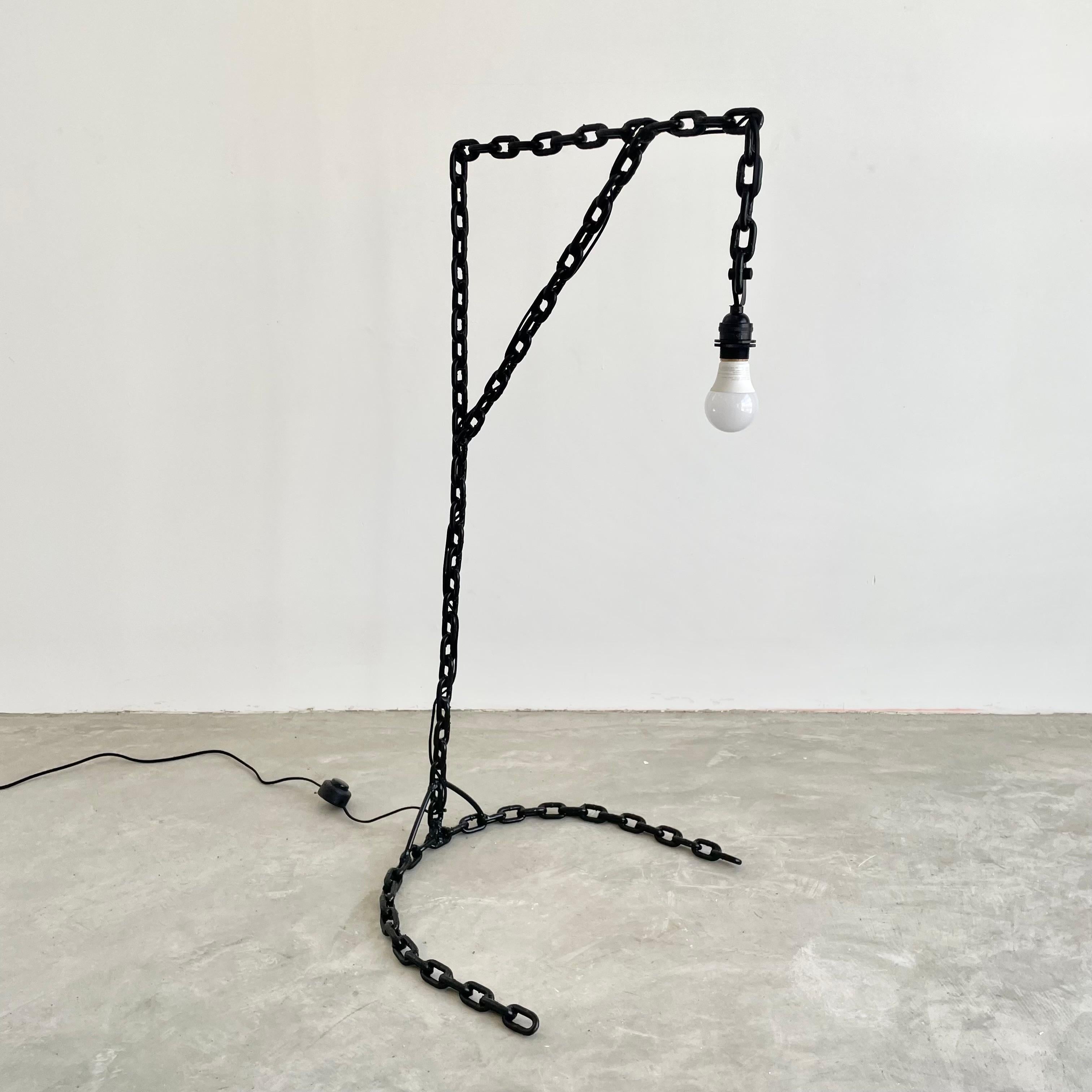 Brutalist iron chain link floor lamp from the UK. Just under 3.5 feet tall. Painted in a jet black paint and made of welded chain link with a cantilever detail making it perfect for low tables or reading chairs. Half moon base with electric cord