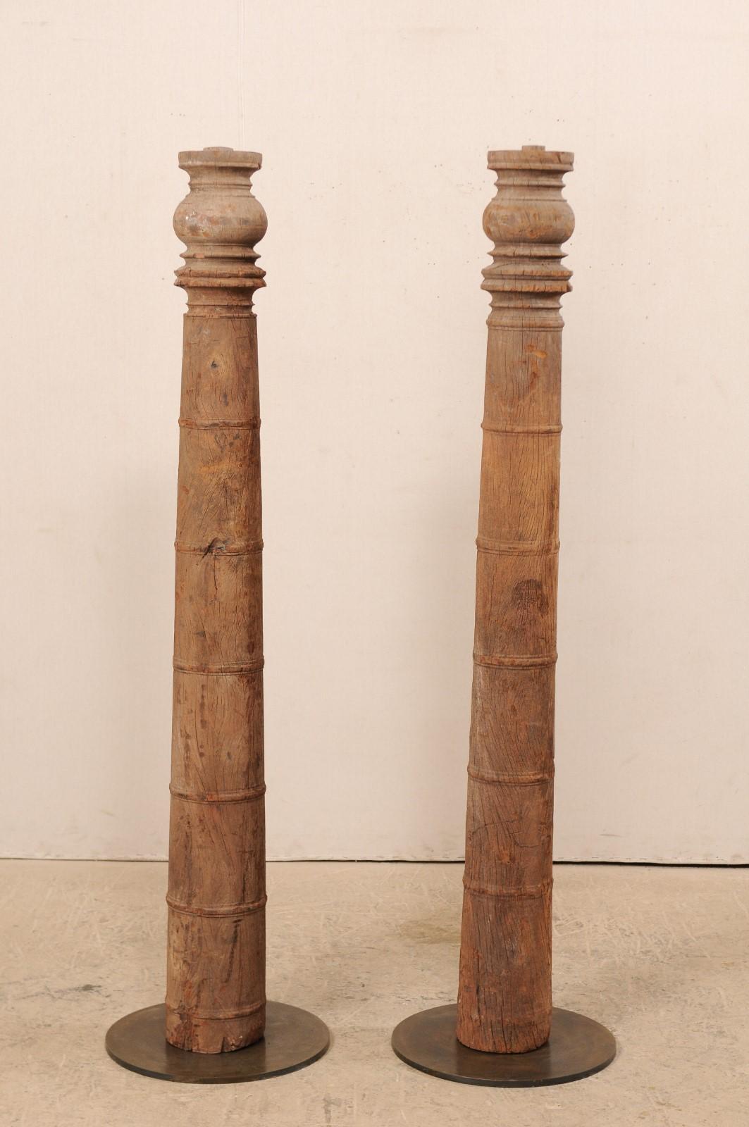A pair of 19th century British Colonial carved wood columns on custom stands. This pair of antique hand carved wooden architectural elements from India, which stand approximately 5.5 feet in height, each feature a rounded column adorn with a series