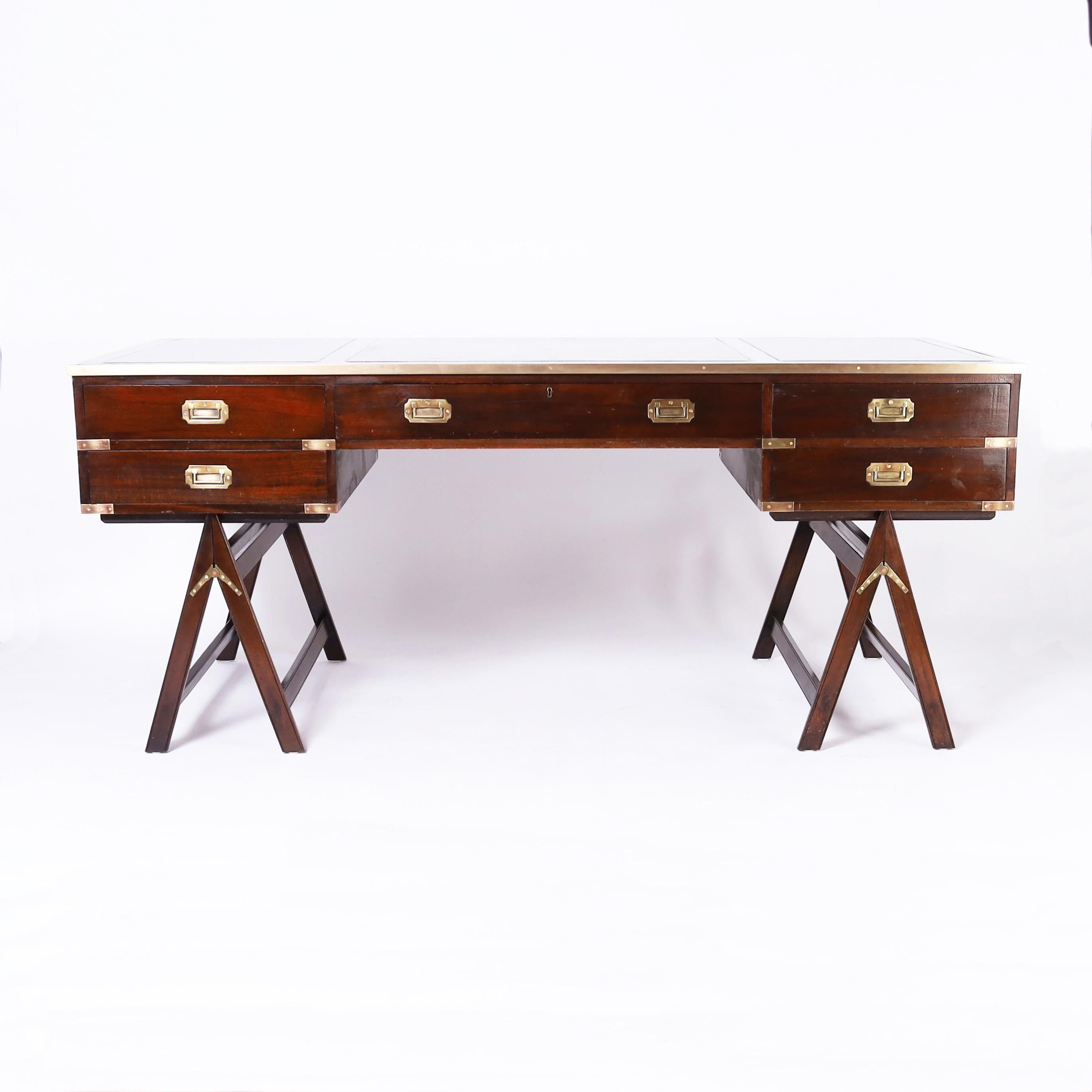 Handsome vintage British Colonial campaign desk with a tooled leather top bound in brass on a five drawer case with brass campaign hardware on two folding sawhorse bases.

Kneehole: 23.5