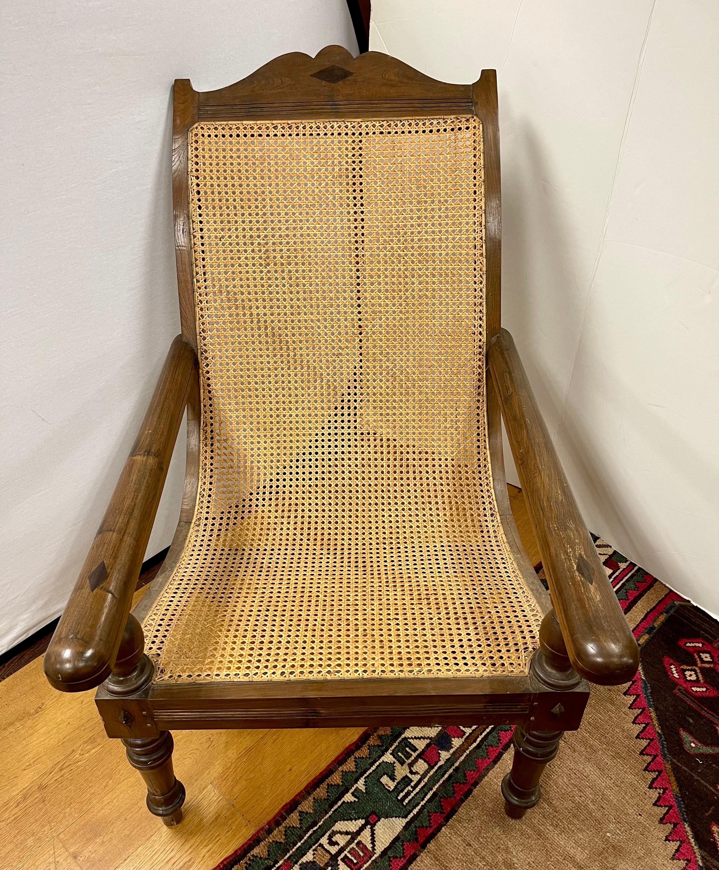 British colonial plantation chair features a carved frame with cane seat and back. Hand made with swing out extension arms that transform into leg rests and can be tucked back under the arms.