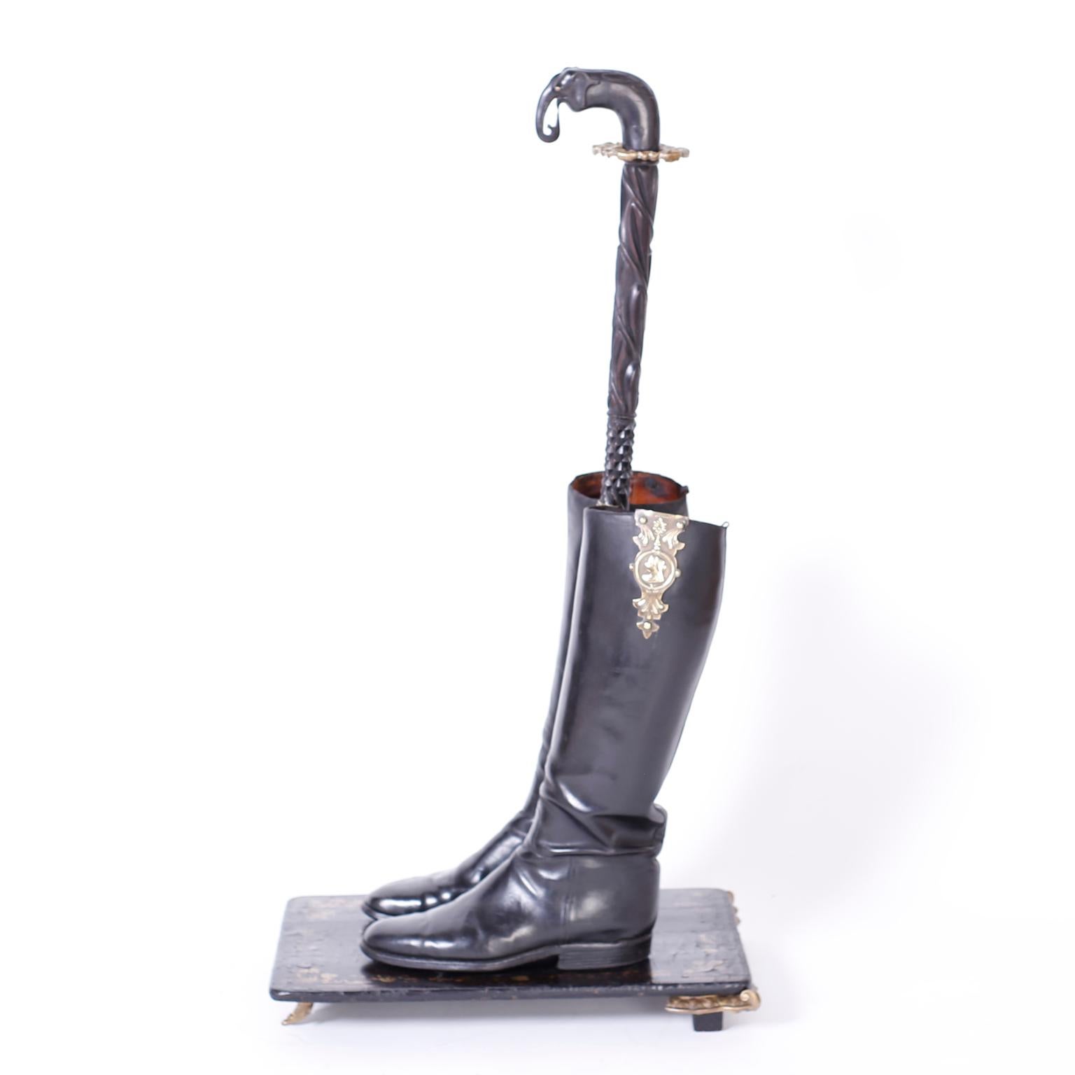 English antique cane or umbrella stand that crosses the line between art and function by assembling two Victorian black leather boots on a Chinese lacquer remnant with antique brass remnants as feet. The handle is an antique Anglo Indian carved cane