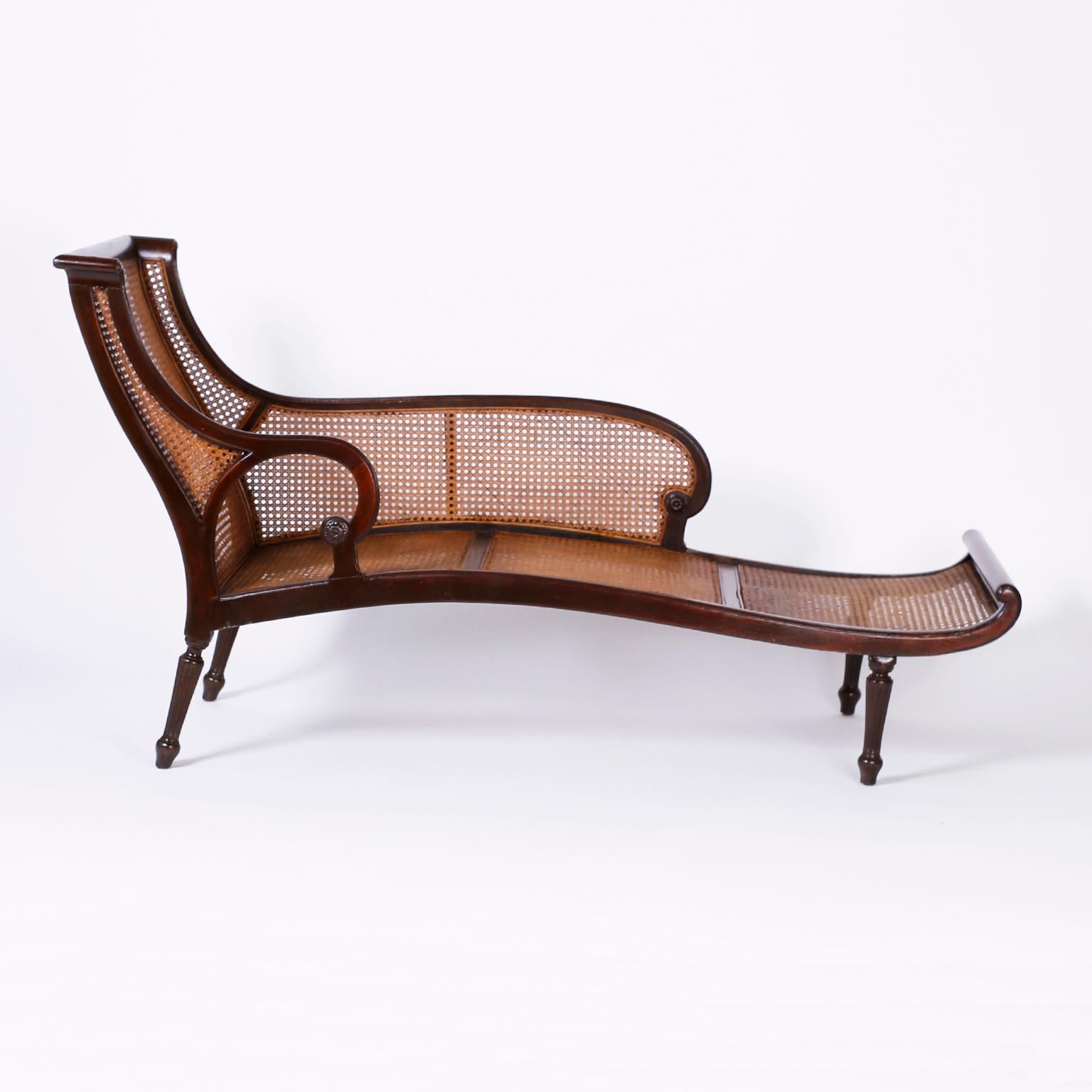 Antique British colonial chaise lounge crafted in mahogany with an elegant art nouveau influenced form, caned back, seat and side, on turned and fluted tapered legs.