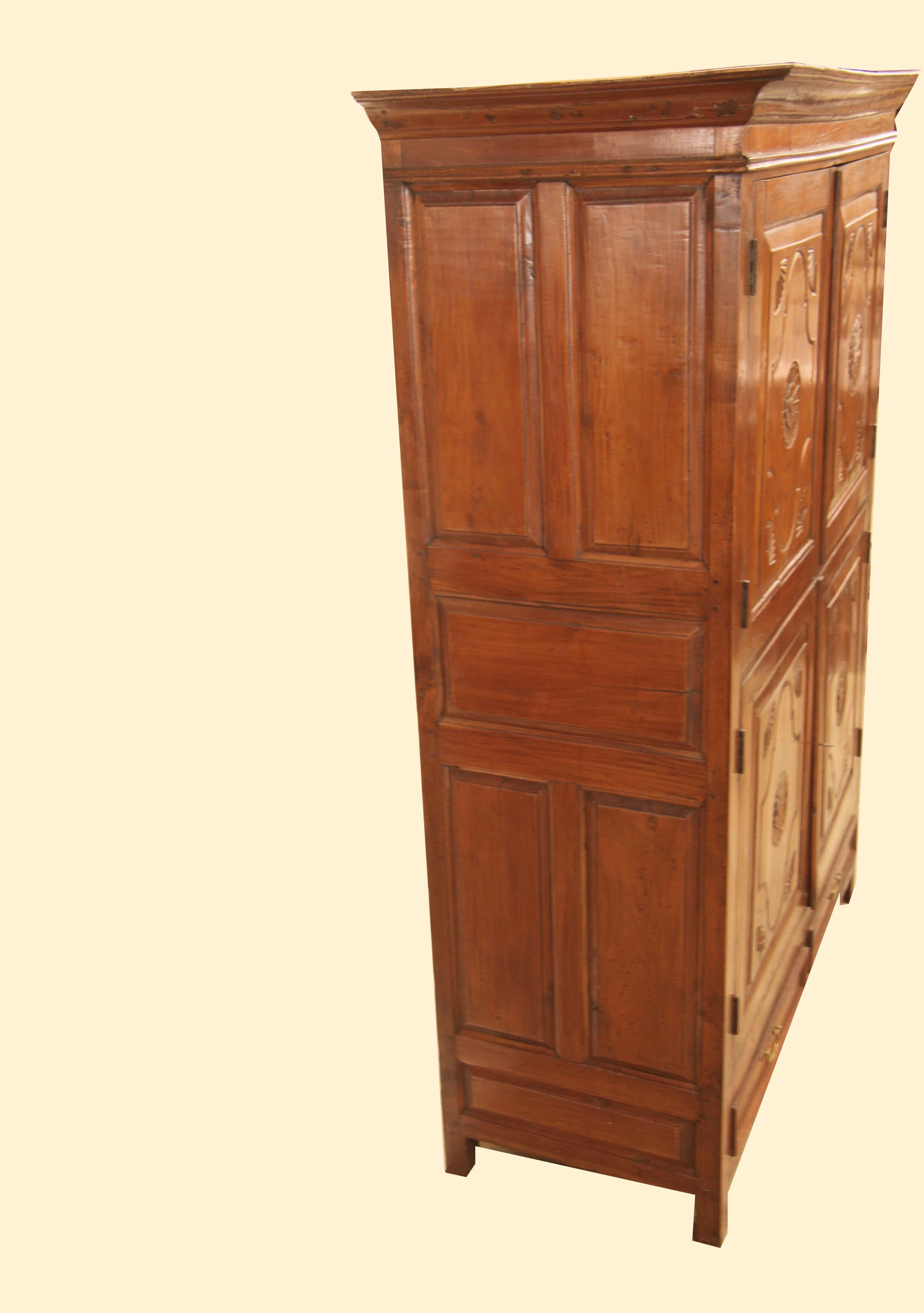 British Colonial carved teak linen press,  with cove cornice above double doors in the top and bottom portion.  The sides have multiple raised panels;  the four raised panel doors feature a large central carved rosette with carved stylized fans in