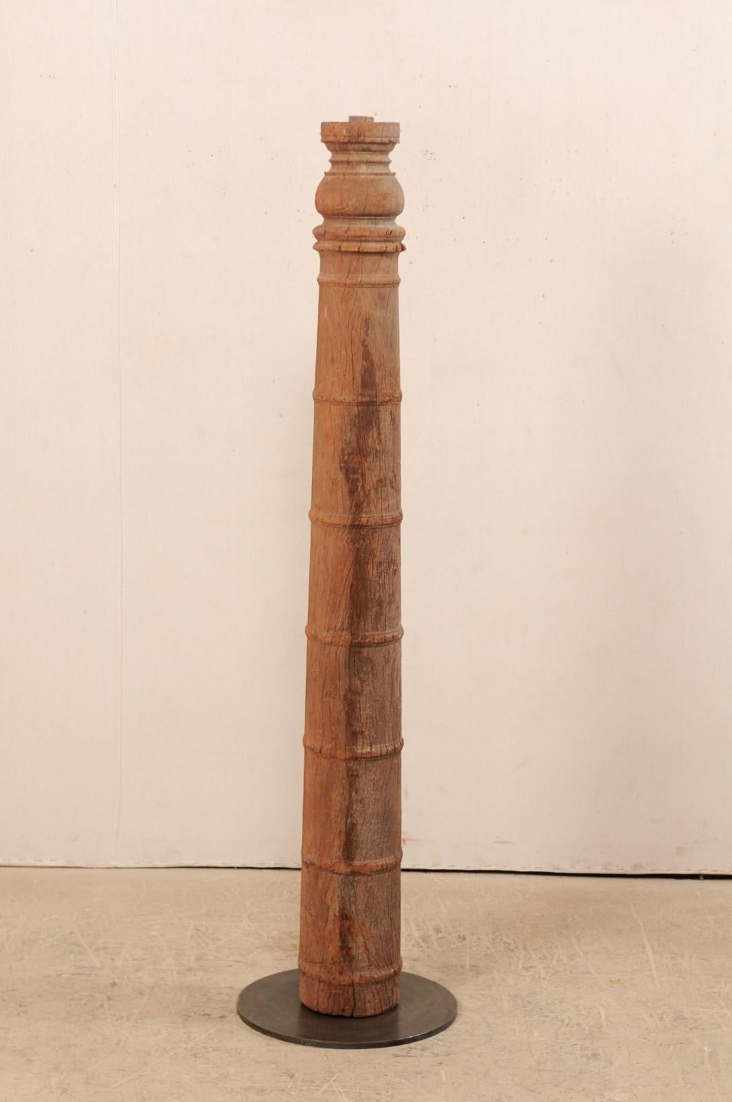 A single 19th century British Colonial carved wood column with custom stand. This antique hand carved wooden architectural element from India, which stands approximately 5.5 feet in height, features a rounded column adorn with a series of carved