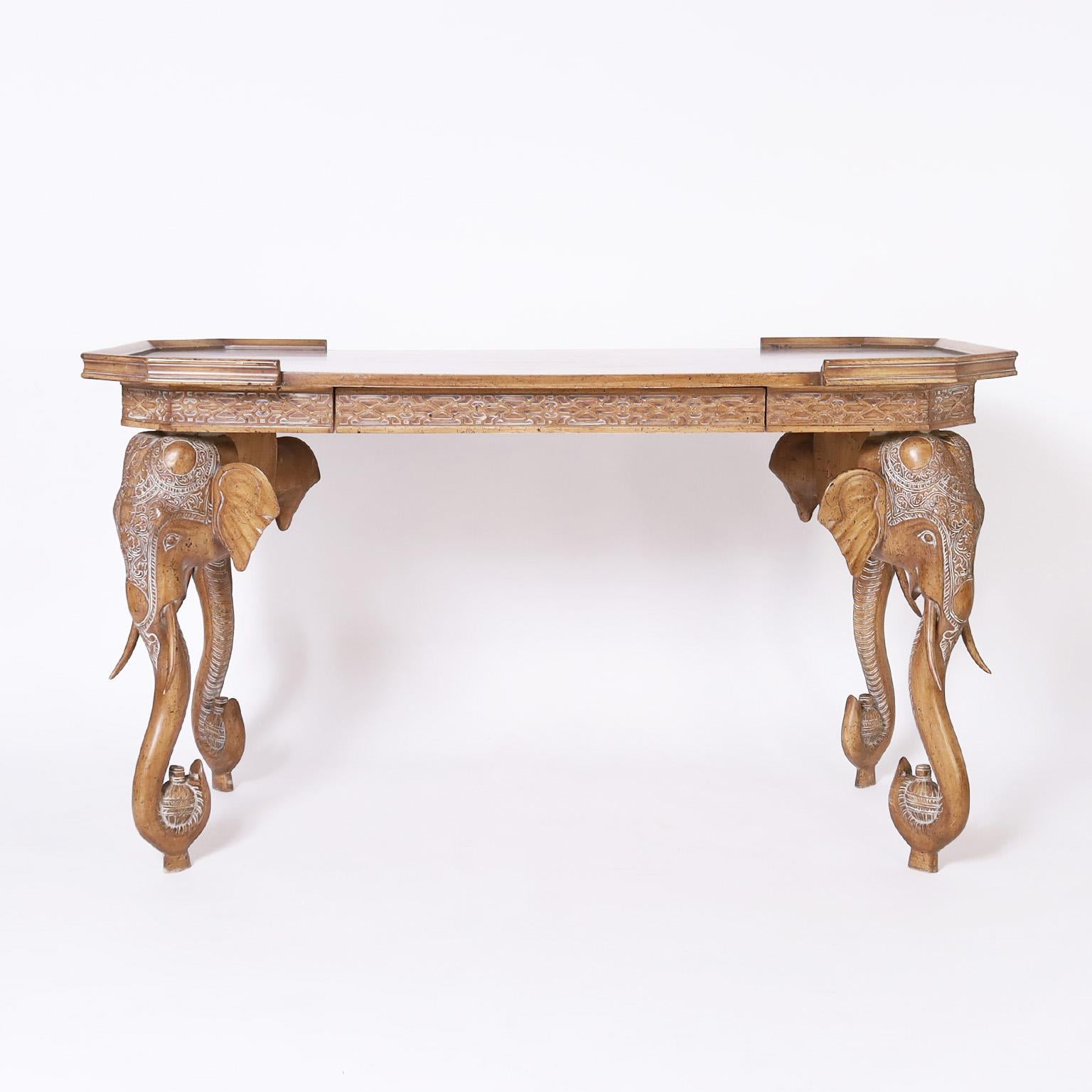 British colonial style one drawer writing desk or table crafted in walnut with a chic pecan finish with contrived aging and featuring four carved elephant head legs with an India inspired motif.