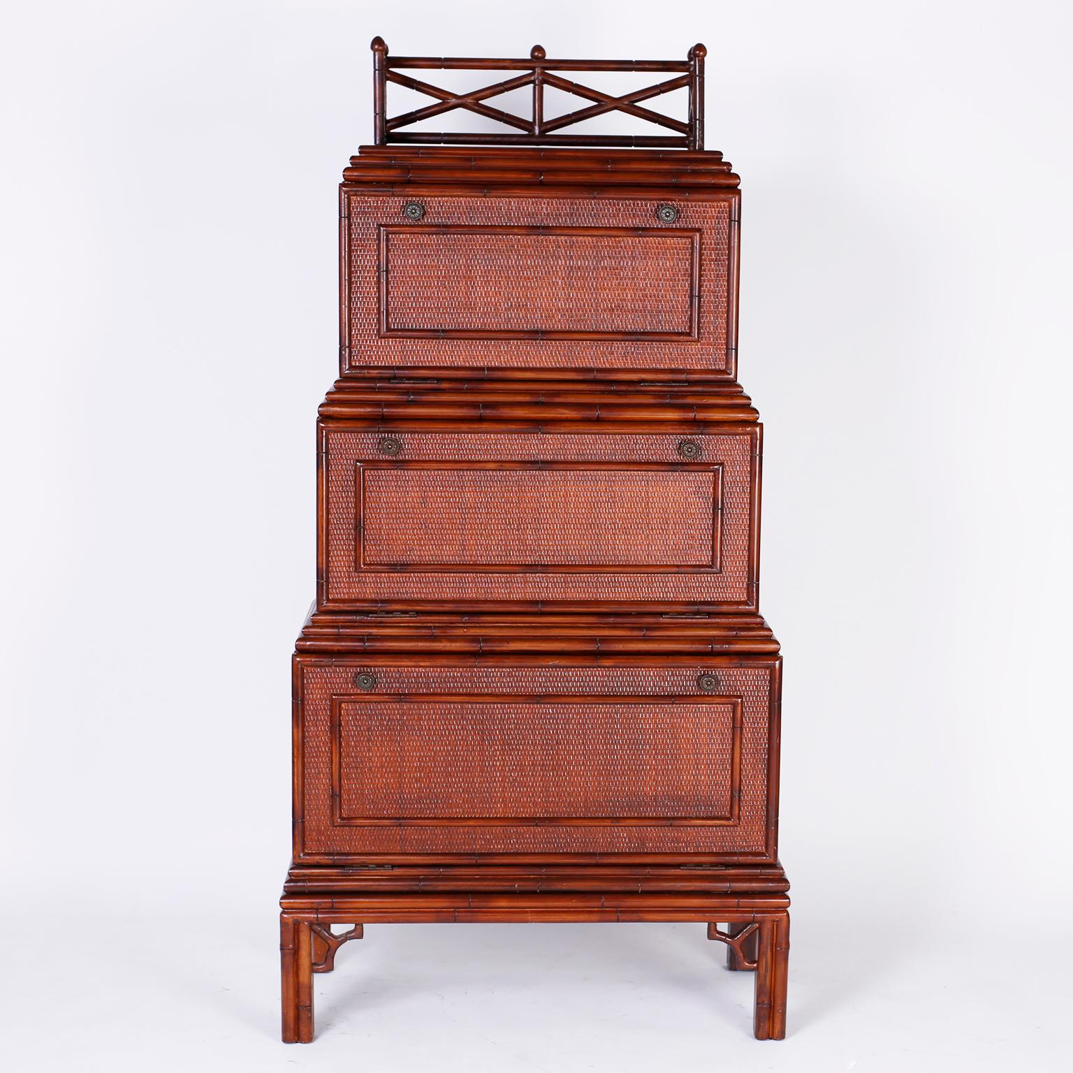 British Colonial style three-tiered cabinet desk with a gallery at the top over three step down compartments covered with grass cloth and framed with faux bamboo. The upper and lower compartments are storage, the middle a desk. The faux bamboo legs