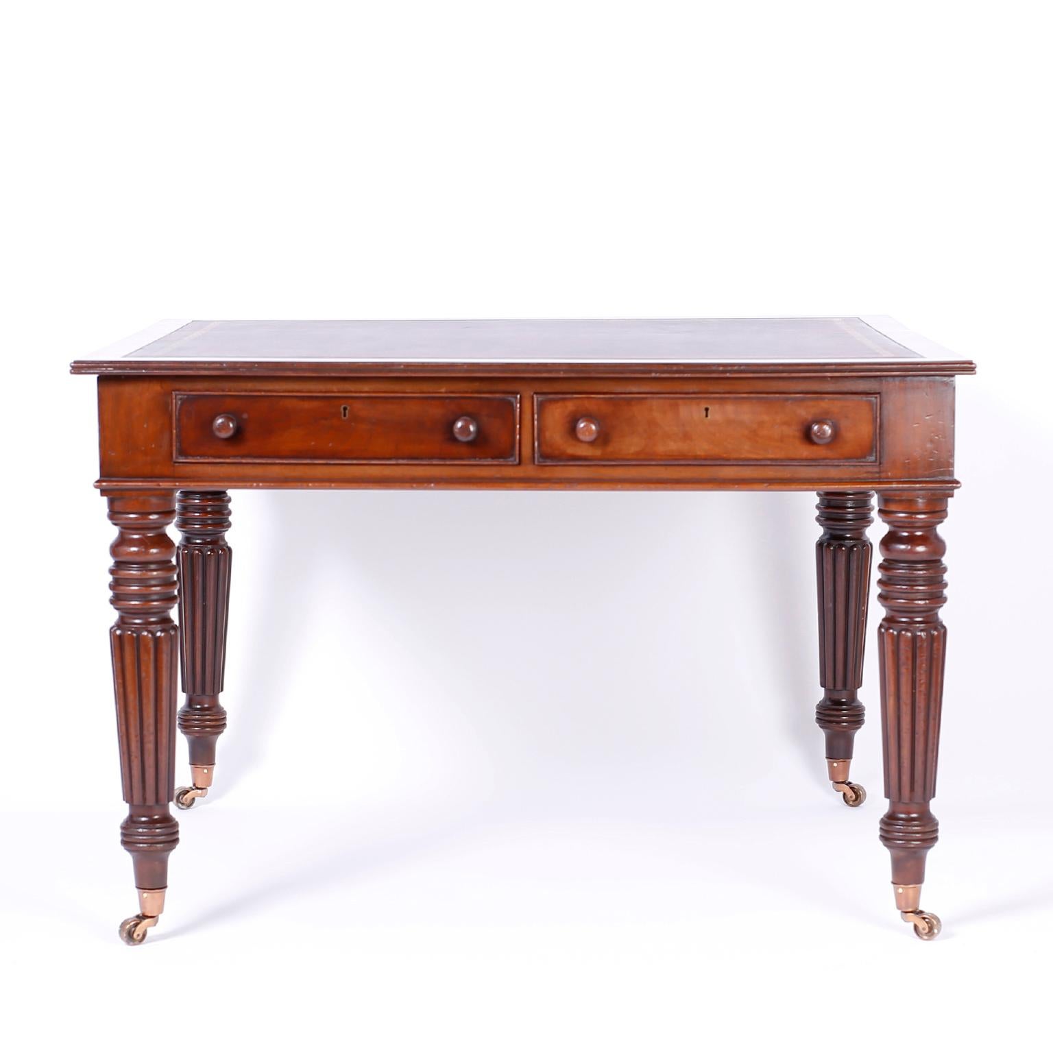 English mahogany partners writing desk with a tooled oxblood leather top, handmade construction, two drawers on each side, and bold turned and beaded legs on brass casters.