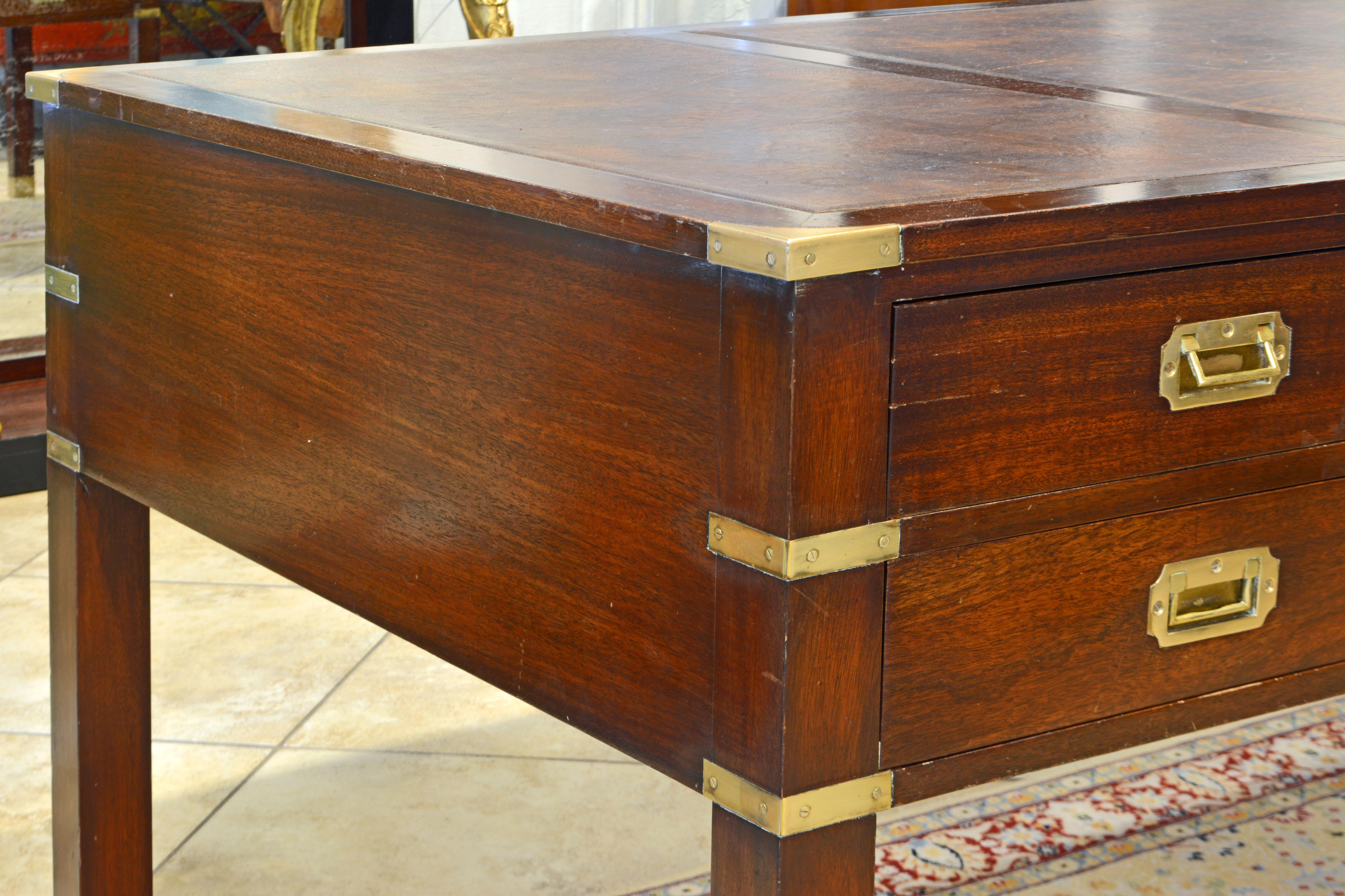 This British Colonial Mahogany campaign style desk features a top with three leather lined panels above five drawers with flush mounted brass handles on one side and simulated drawers on the other. The joints are accented by flush mounted brass