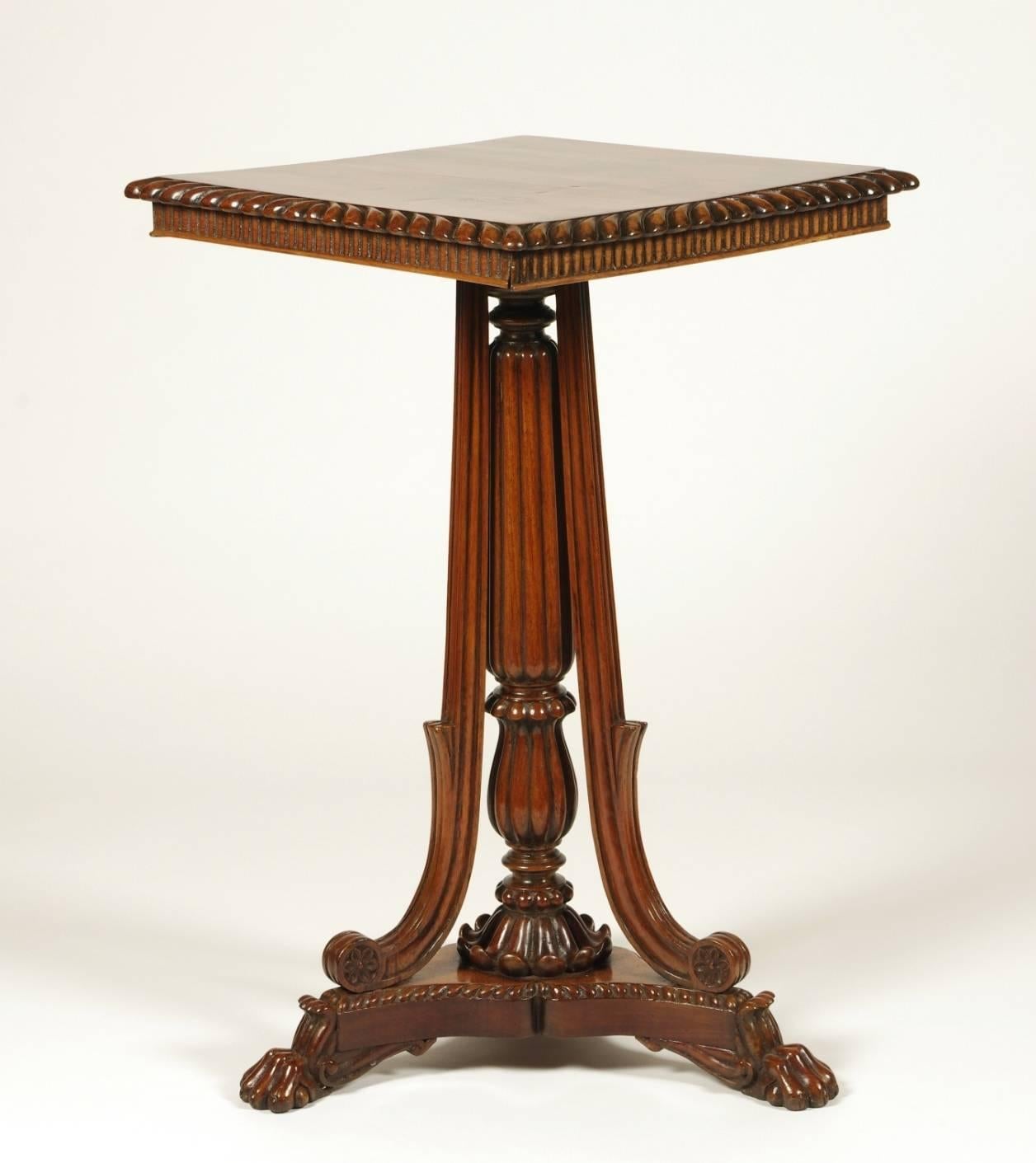 British Colonial padouk wood tilt top side table, the square top with gadrooned edges and fluted apron on the reeded post with three carved supports on a triangular base with paw feet.

Similar tables with center posts and applied supports are